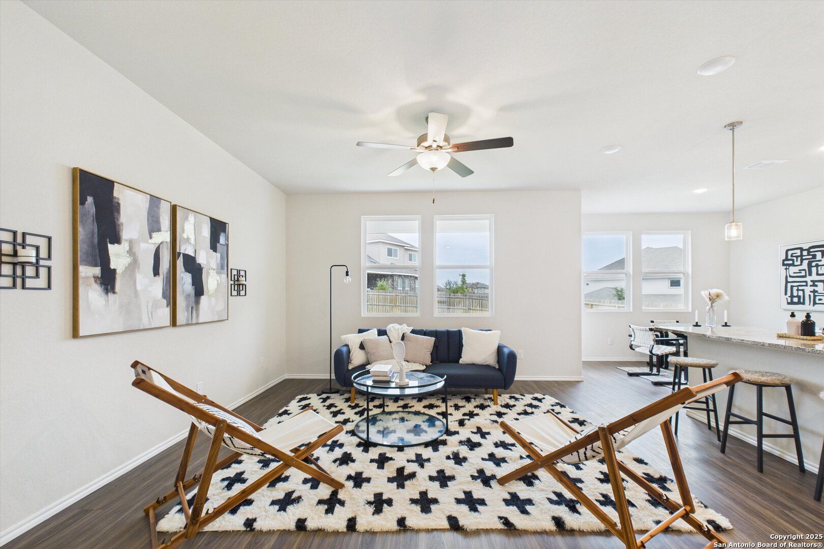 Modern living room with navy velvet sofa, glass coffee table, abstract art, and open kitchen in Davidson Homes Asheville K, Bricewood, San Antonio