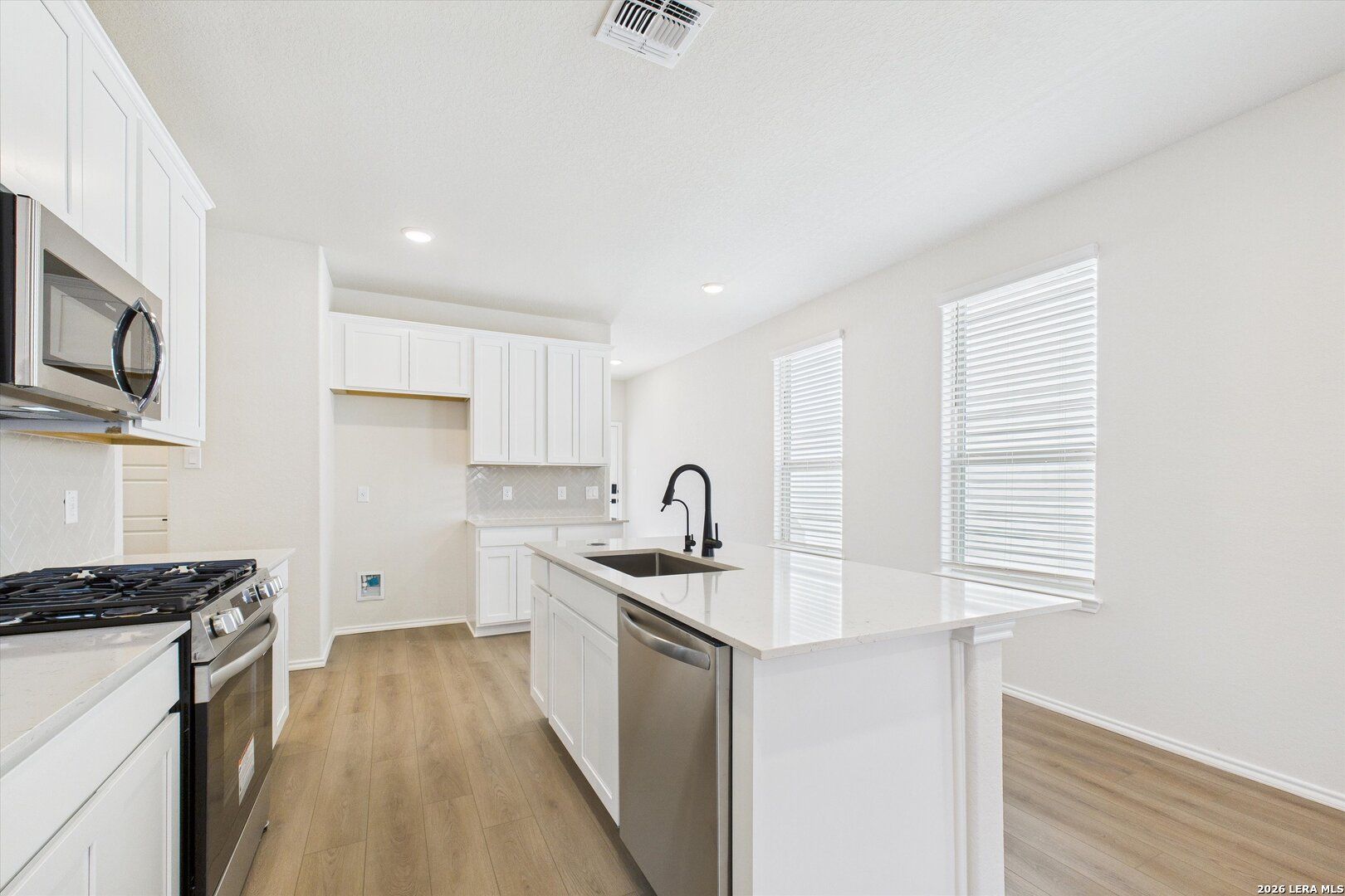 Bright modern kitchen with white cabinets, stainless steel appliances, quartz island, and hardwood floors in The Gillian B, San Antonio, Texas