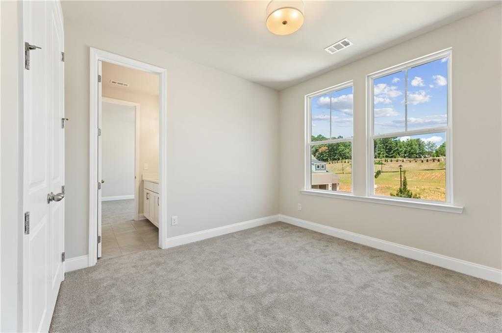 Bright secondary bedroom with neutral walls, carpet flooring, large windows overlooking fields, en-suite bath in 5-bed Davidson Homes The Hampton C, Buford, GA