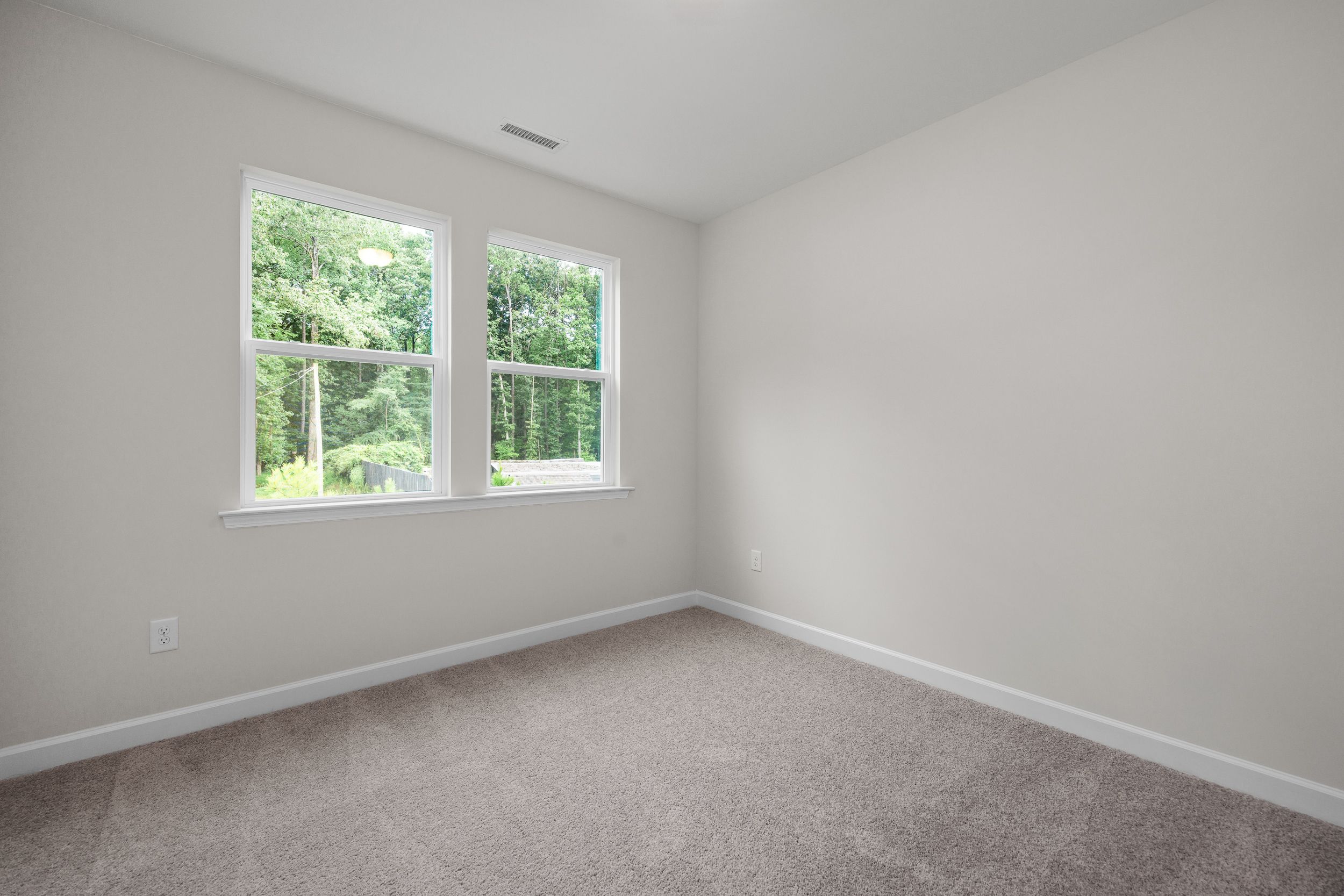 Spacious secondary bedroom in The Aspen Davidson Homes design with large windows overlooking wooded views and neutral beige walls