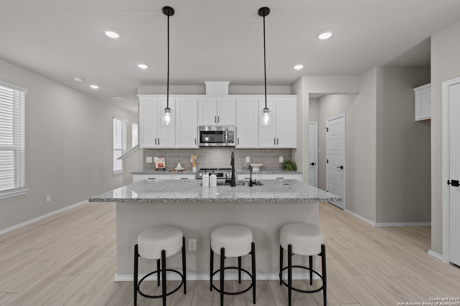 Modern open-concept kitchen with granite island, white cabinets, bar stools, and pendant lights in The Charlotte B, San Antonio