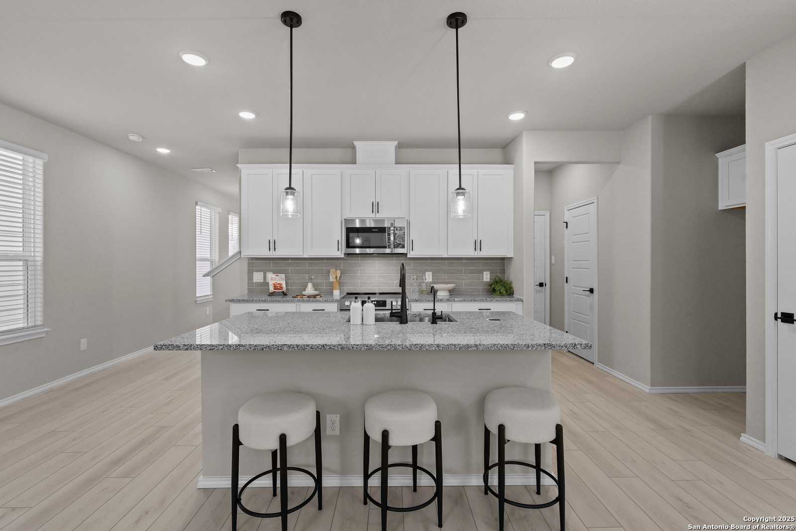Modern open-concept kitchen with granite island, white cabinets, bar stools, and pendant lights in The Charlotte B, San Antonio