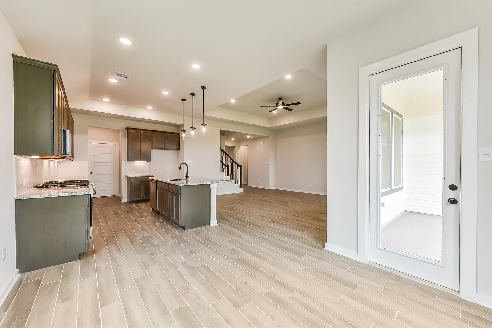 Modern kitchen with gray shaker cabinets, quartz island, gas range, and open living area to covered patio in Davidson Homes Sequoia C, Crosby, TX