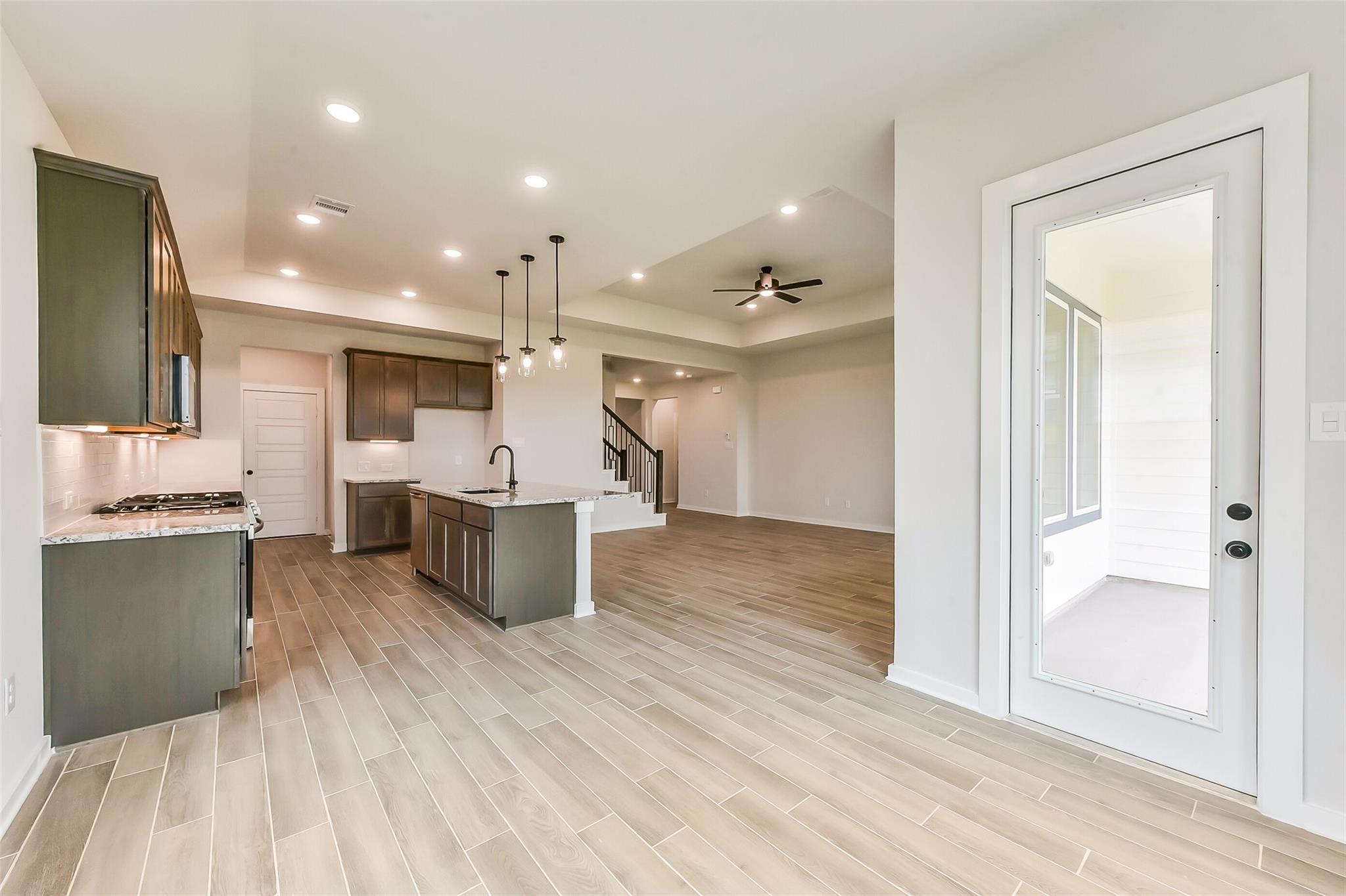 Modern kitchen with gray shaker cabinets, quartz island, gas range, and open living area to covered patio in Davidson Homes Sequoia C, Crosby, TX