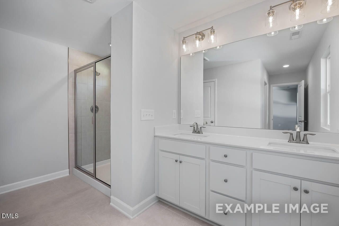 Modern master bathroom with double white vanity, large mirror, and frameless glass shower in Davidson Homes The Adalynn A, Lillington, NC
