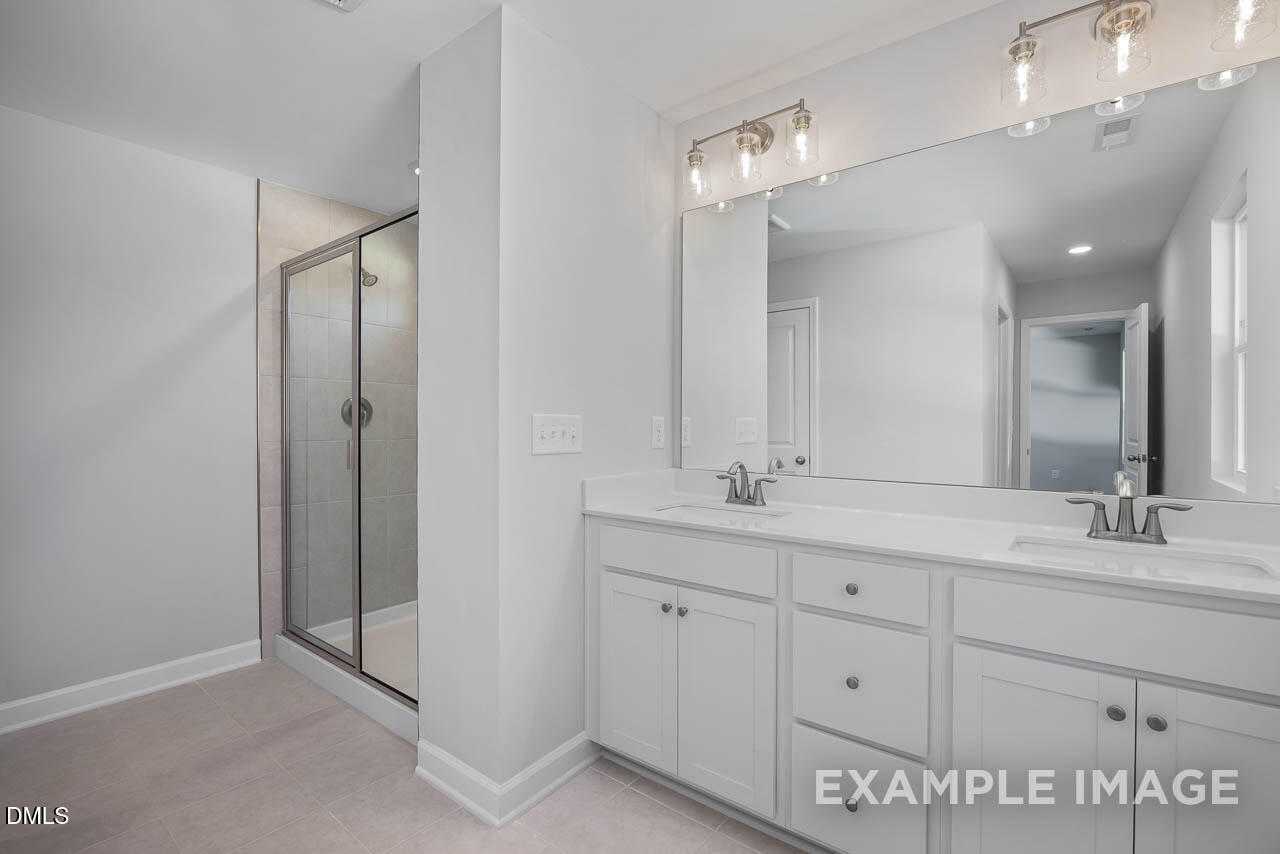 Modern master bathroom with double white vanity, large mirror, and frameless glass shower in Davidson Homes The Adalynn A, Lillington, NC