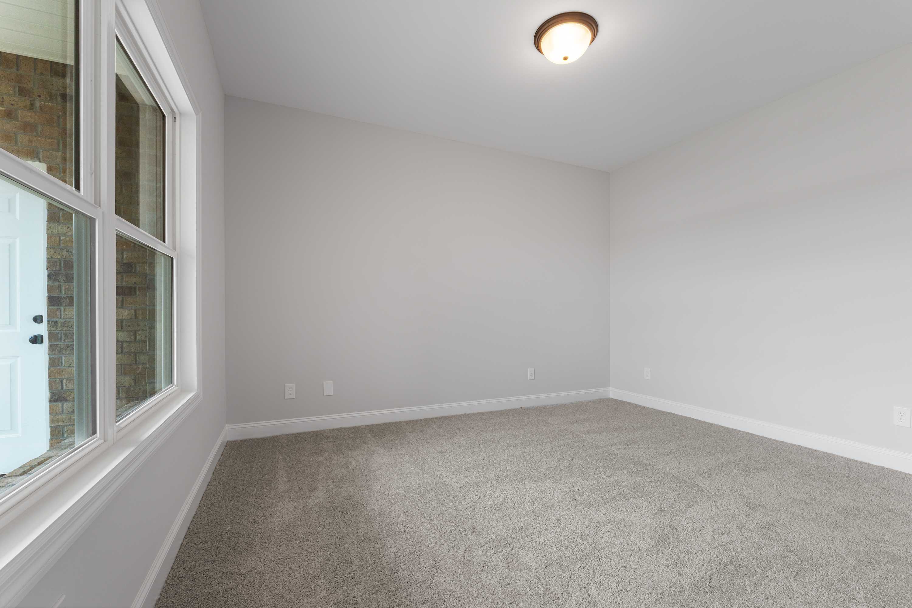 Spacious empty bedroom in The Copeland home with gray carpet, white walls, large window, and flush-mount ceiling light