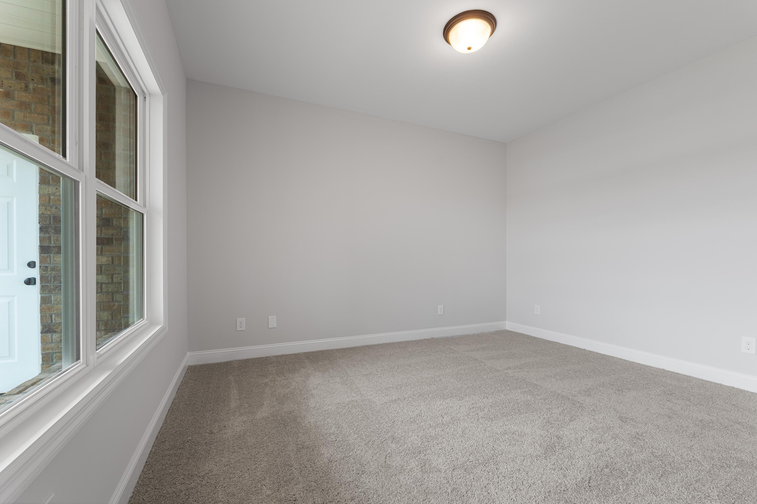 Spacious empty bedroom in The Copeland by Davidson Homes, Madison AL, with neutral walls, carpet floor, large window, ceiling light