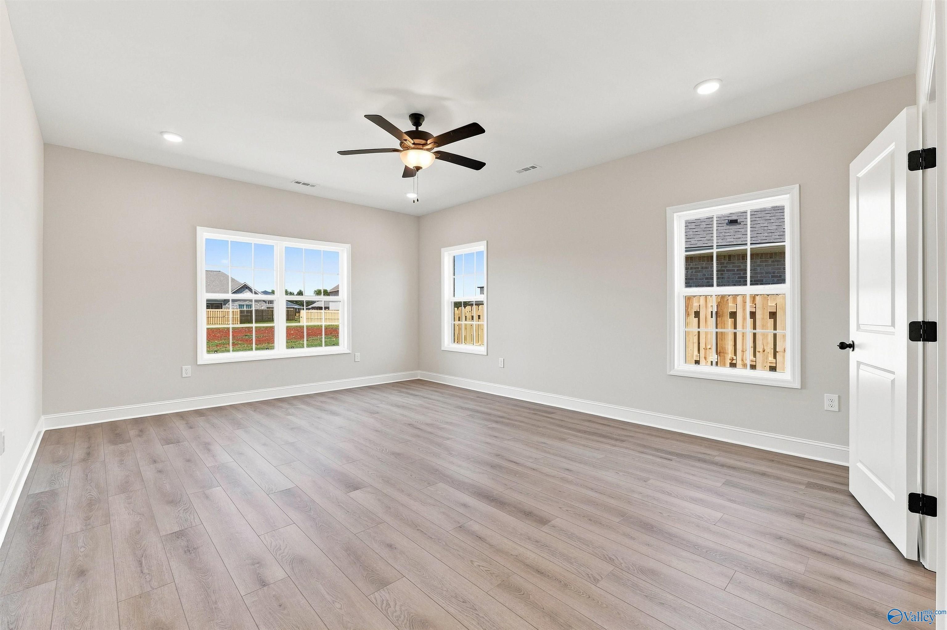 Spacious secondary bedroom with light wood-style flooring and ceiling fan in The Oxford floor plan, Kendall Farms, Toney, AL.