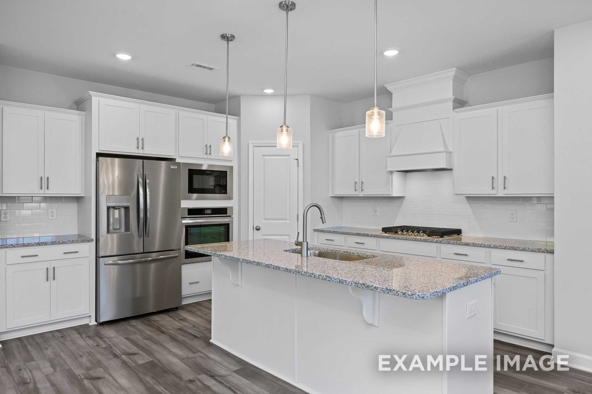 Modern kitchen in The Preston B showcasing white shaker cabinets, large island with sink, stainless steel appliances, subway tile backsplash