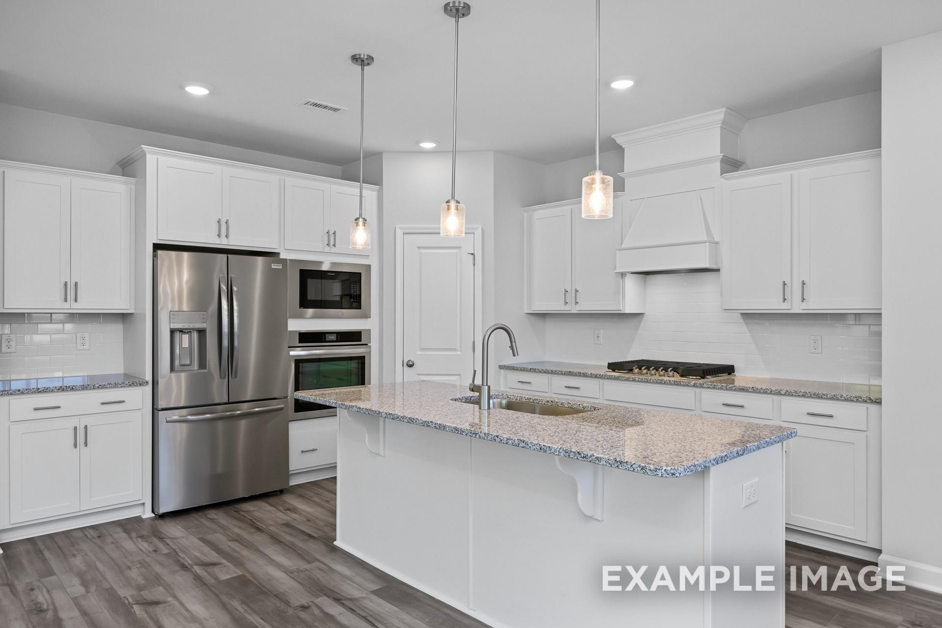 Modern kitchen in The Preston B showcasing white shaker cabinets, large island with sink, stainless steel appliances, subway tile backsplash