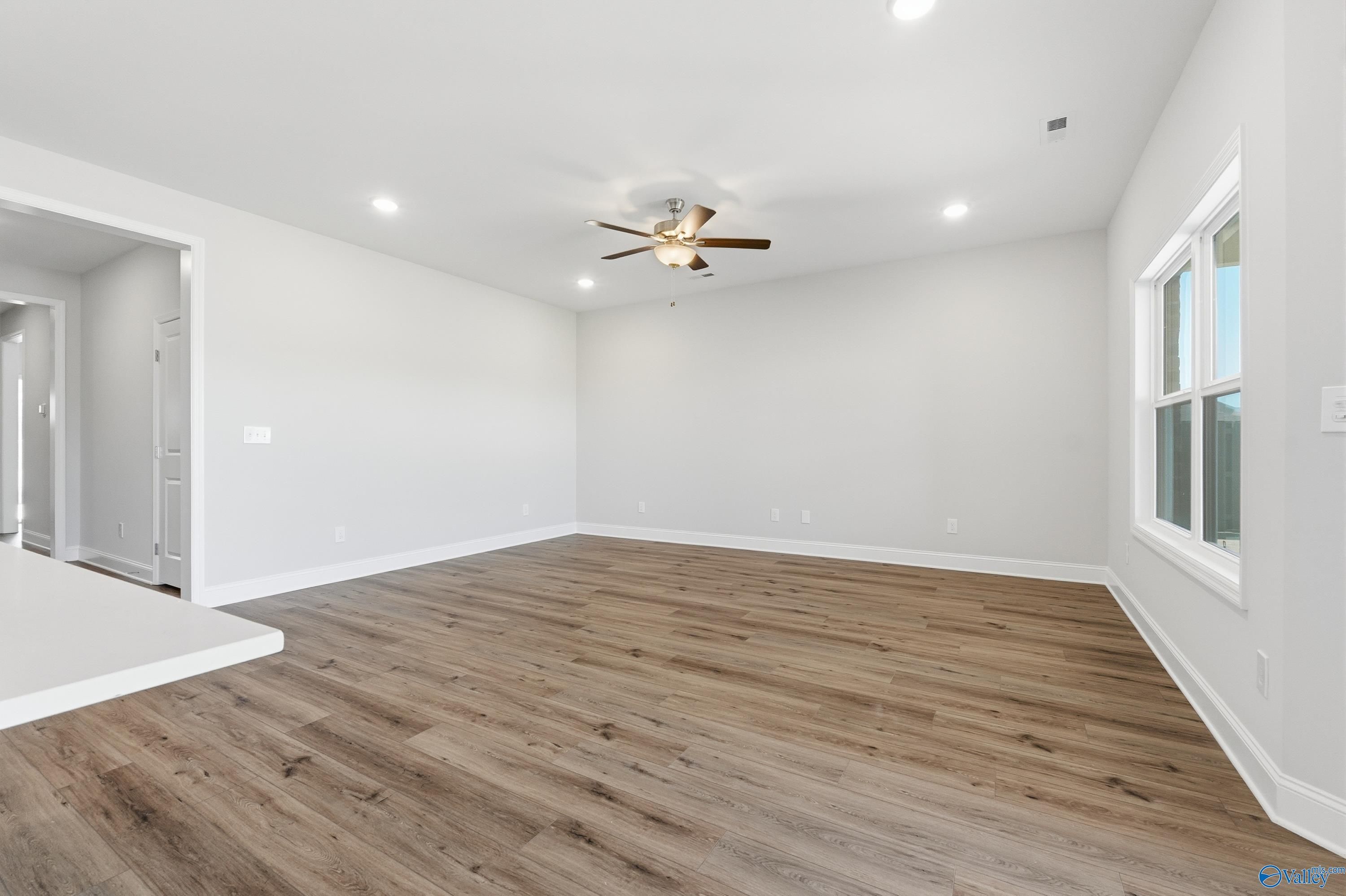 Spacious great room with ceiling fan, luxury vinyl plank floors, large windows, and open layout in The Everett plan by Davidson Homes, Harvest AL