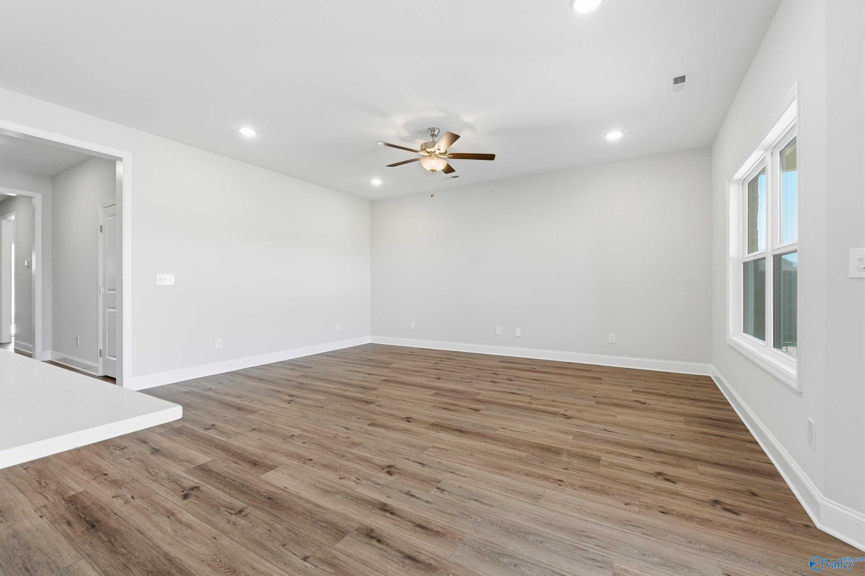 Spacious great room with ceiling fan, luxury vinyl plank floors, large windows, and open layout in The Everett plan by Davidson Homes, Harvest AL