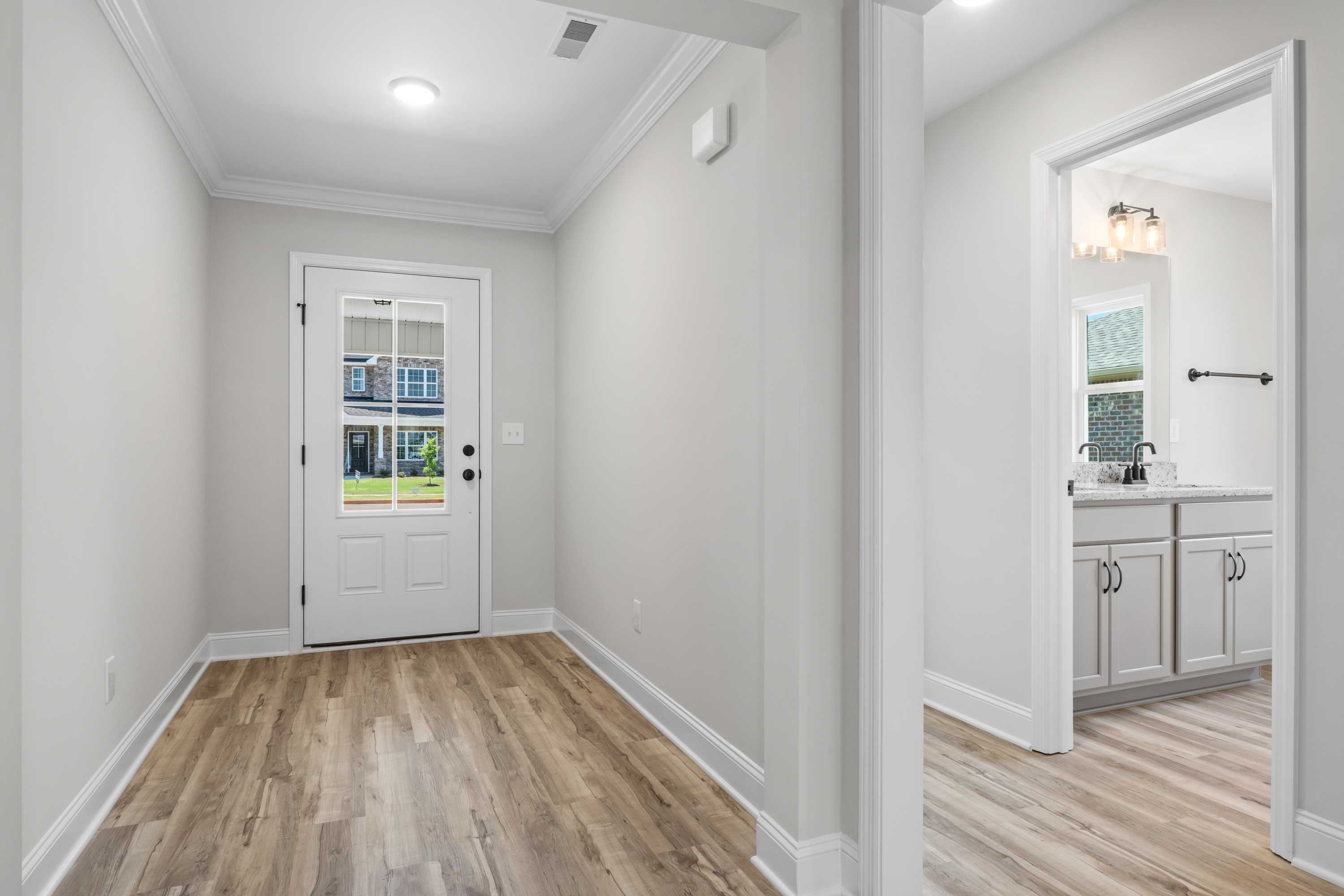 Spacious hallway and modern bathroom in The Everett C home with gray walls, hardwood floors, glass-paneled door, and white vanity
