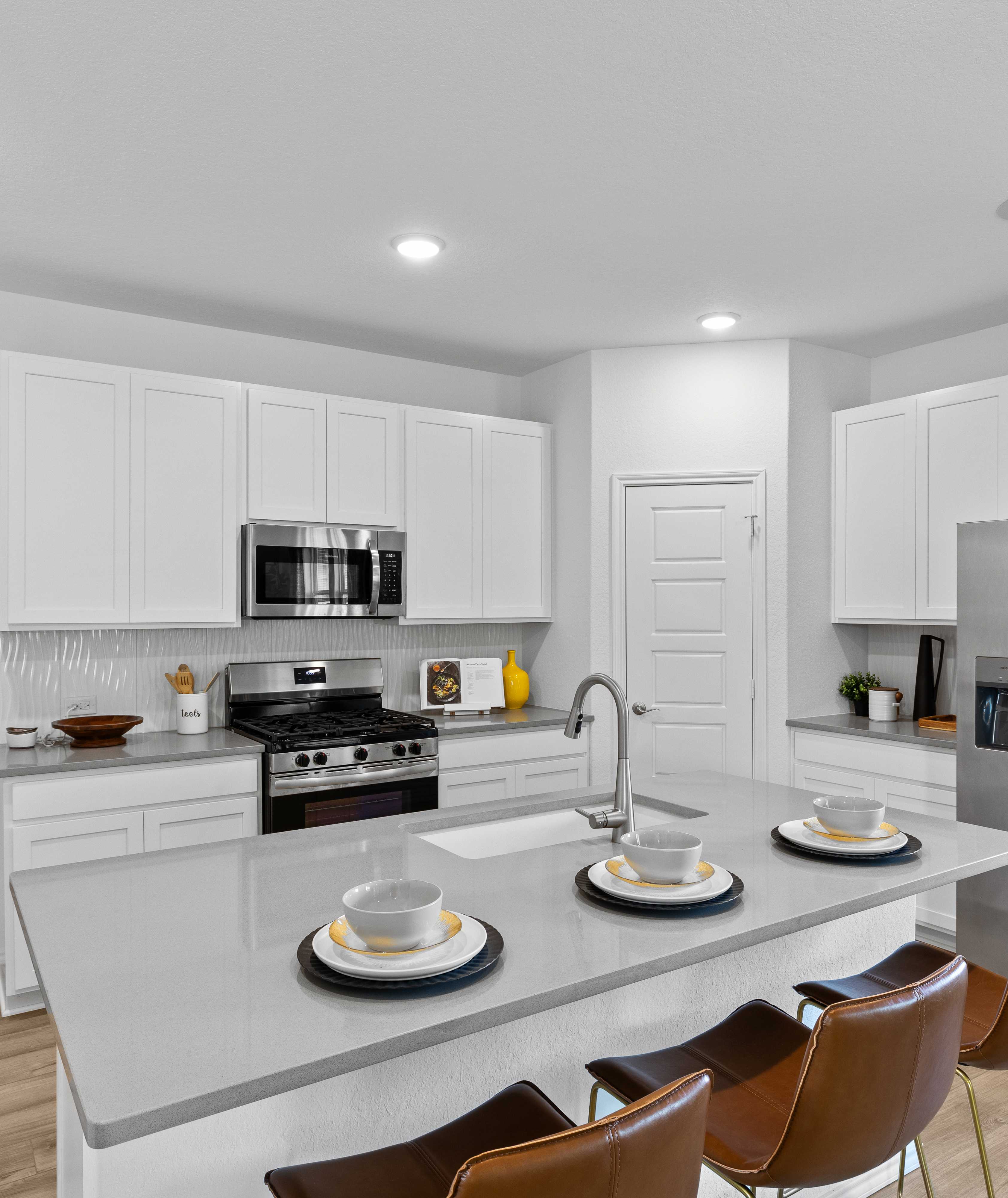 Spacious modern kitchen in Horizon Pointe Converse Texas with white shaker cabinets quartz island stainless appliances hardwood floors