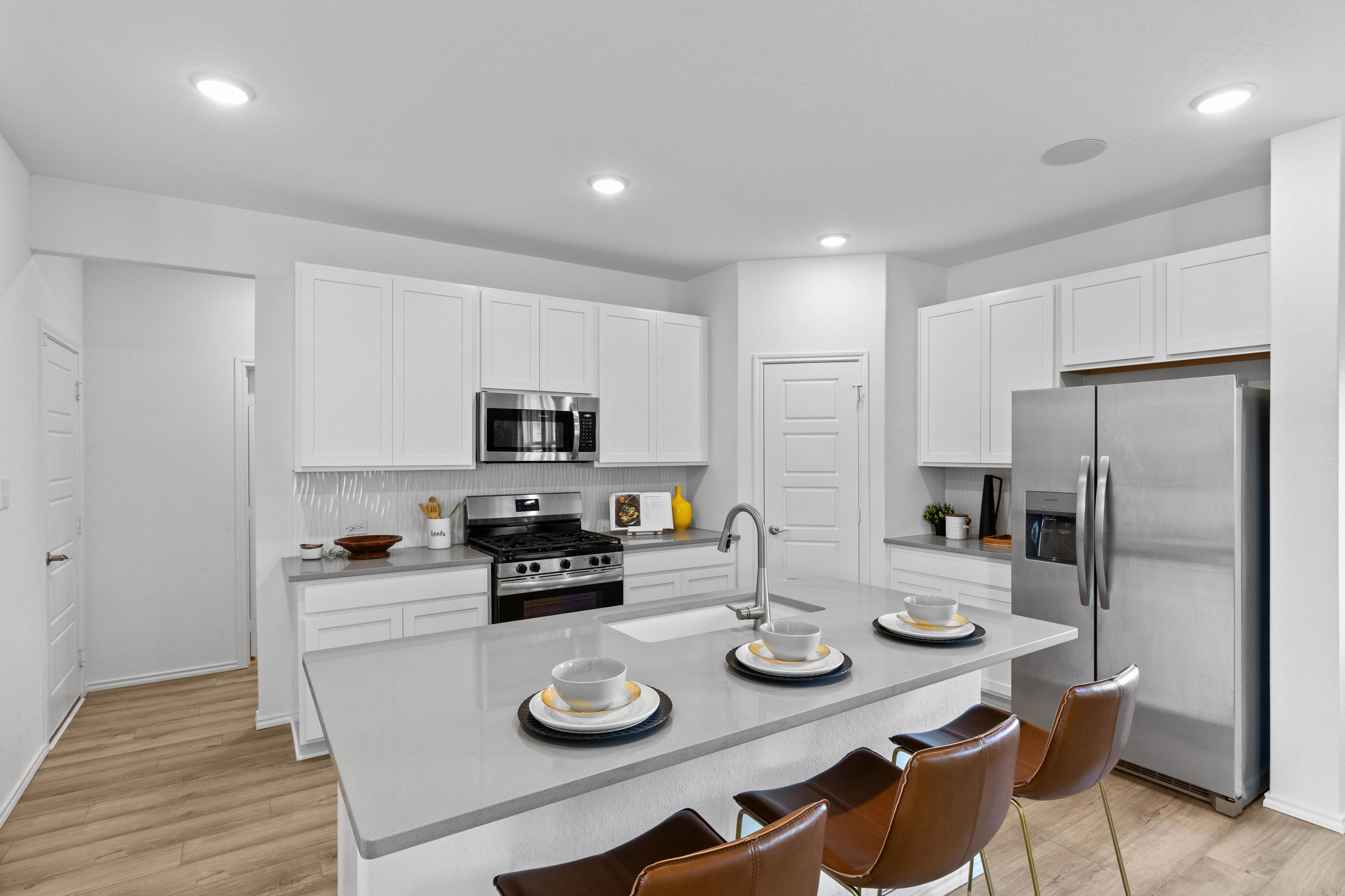 Spacious modern kitchen in Horizon Pointe Converse Texas with white shaker cabinets quartz island stainless appliances hardwood floors