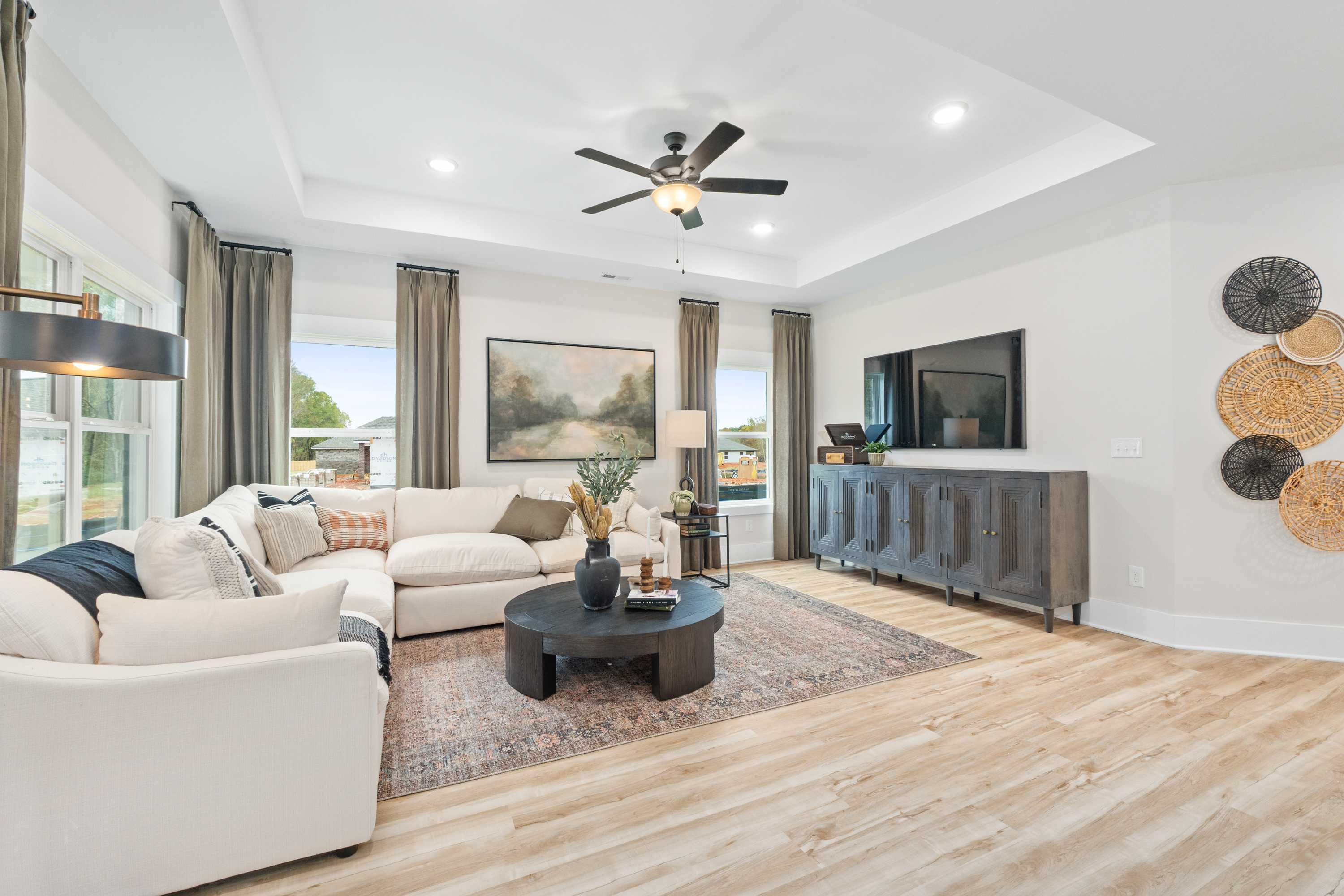 Spacious living room in Spragins Cove Huntsville AL with beige L-shaped sofa, hardwood floors, ceiling fan, and large curtained windows