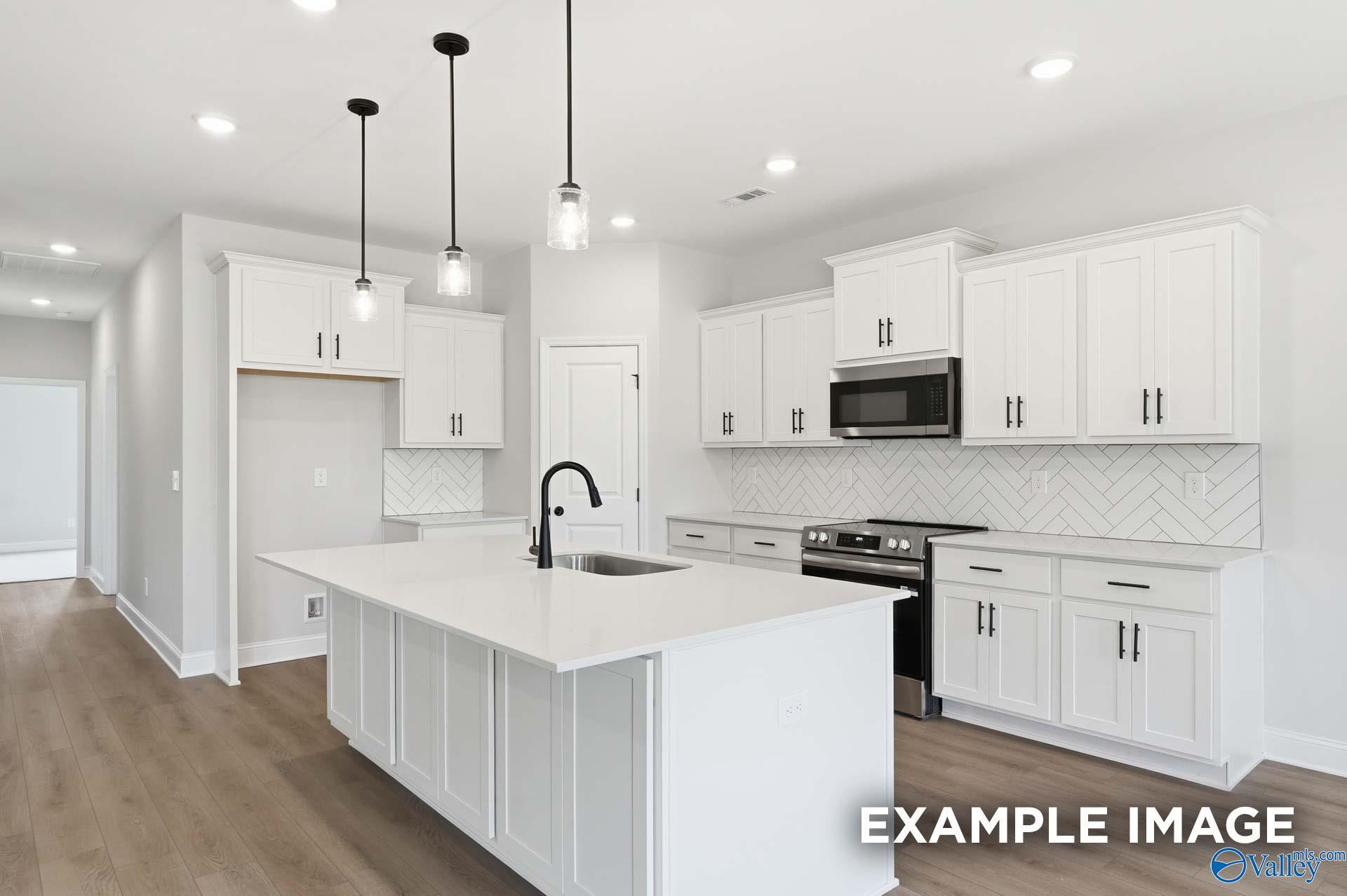 Modern white kitchen with quartz island, herringbone backsplash, and pendant lighting in The Rockford C, Evergreen Mill.