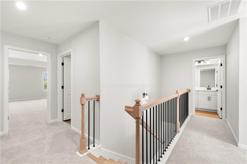 Spacious upstairs hallway with wooden staircase, black railings, and adjacent bathroom in Davidson Homes The Cary A, Winder, Georgia