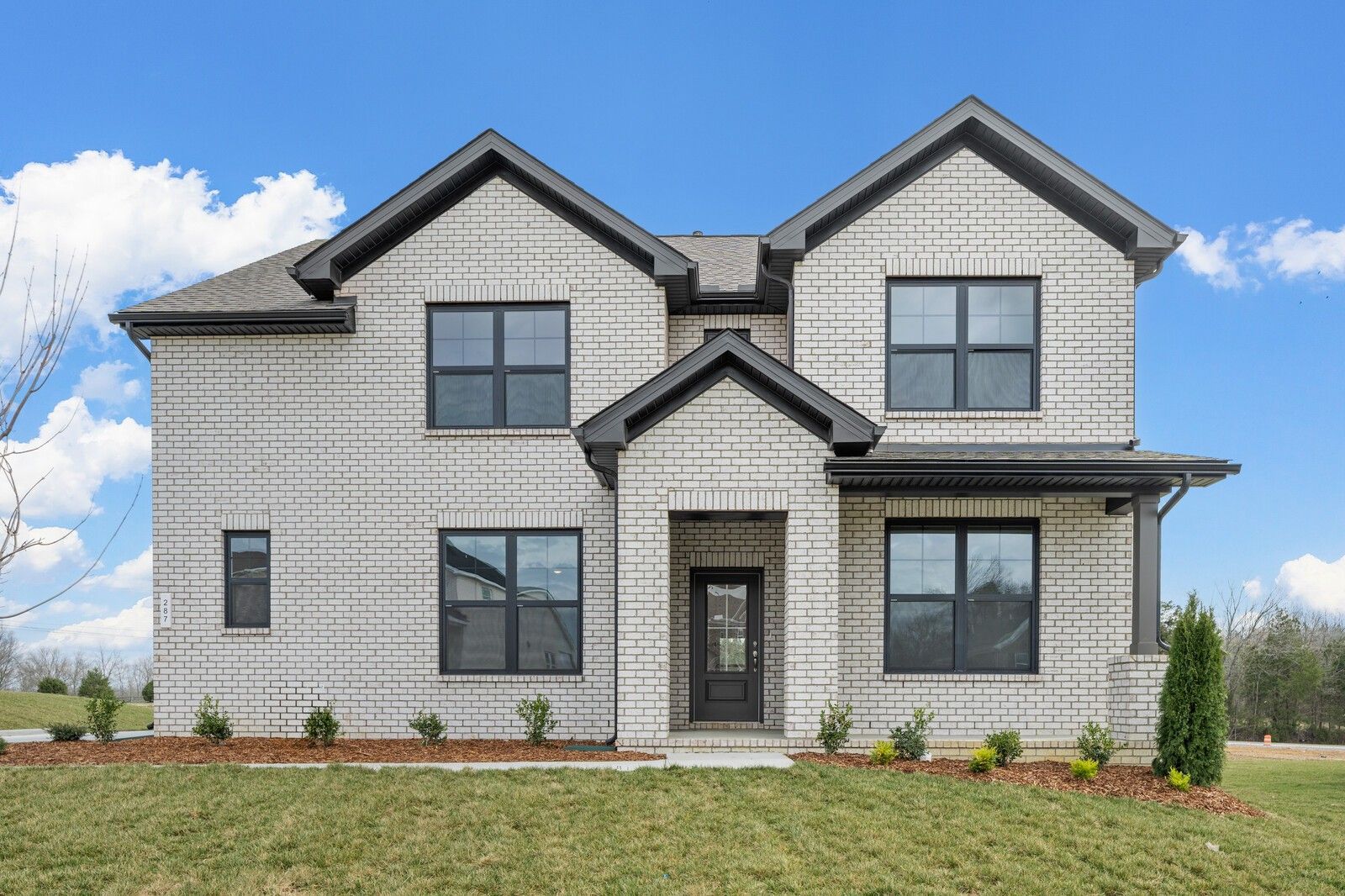 Modern two-story white brick home with black trim, large windows, covered porch, and landscaped yard in Benders Cove, Mt. Juliet