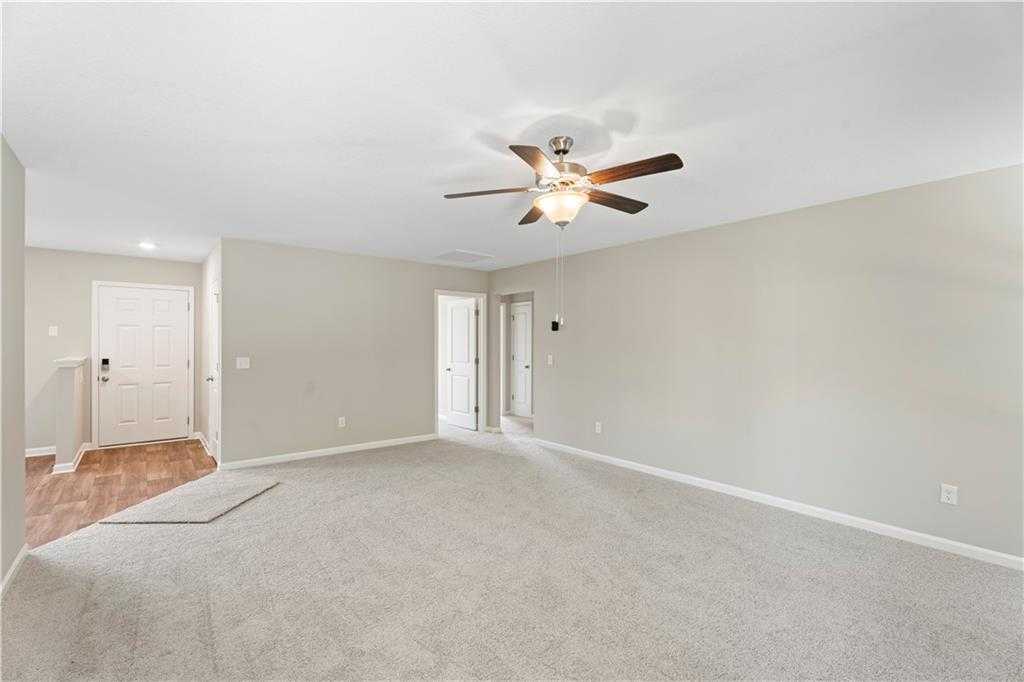 Spacious empty living room with beige walls, light carpet, ceiling fan, and interior doors in The Washington 3-bedroom home, Phenix City, Alabama