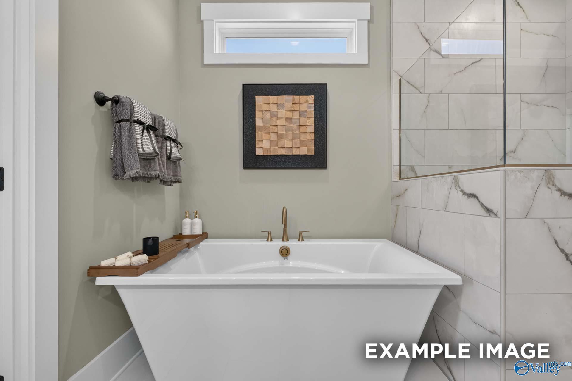 Freestanding soaking tub with brushed gold fixtures beside marble-tiled walk-in shower in primary bath at Forest Glen, Hazel Green, Alabama