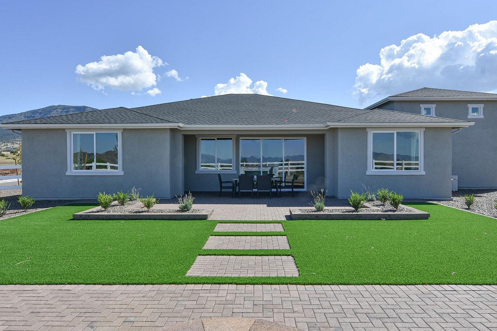 Contemporary single-story exterior of The Summit E home featuring gray stucco, large windows, covered patio, and lush yard in Prescott Valley