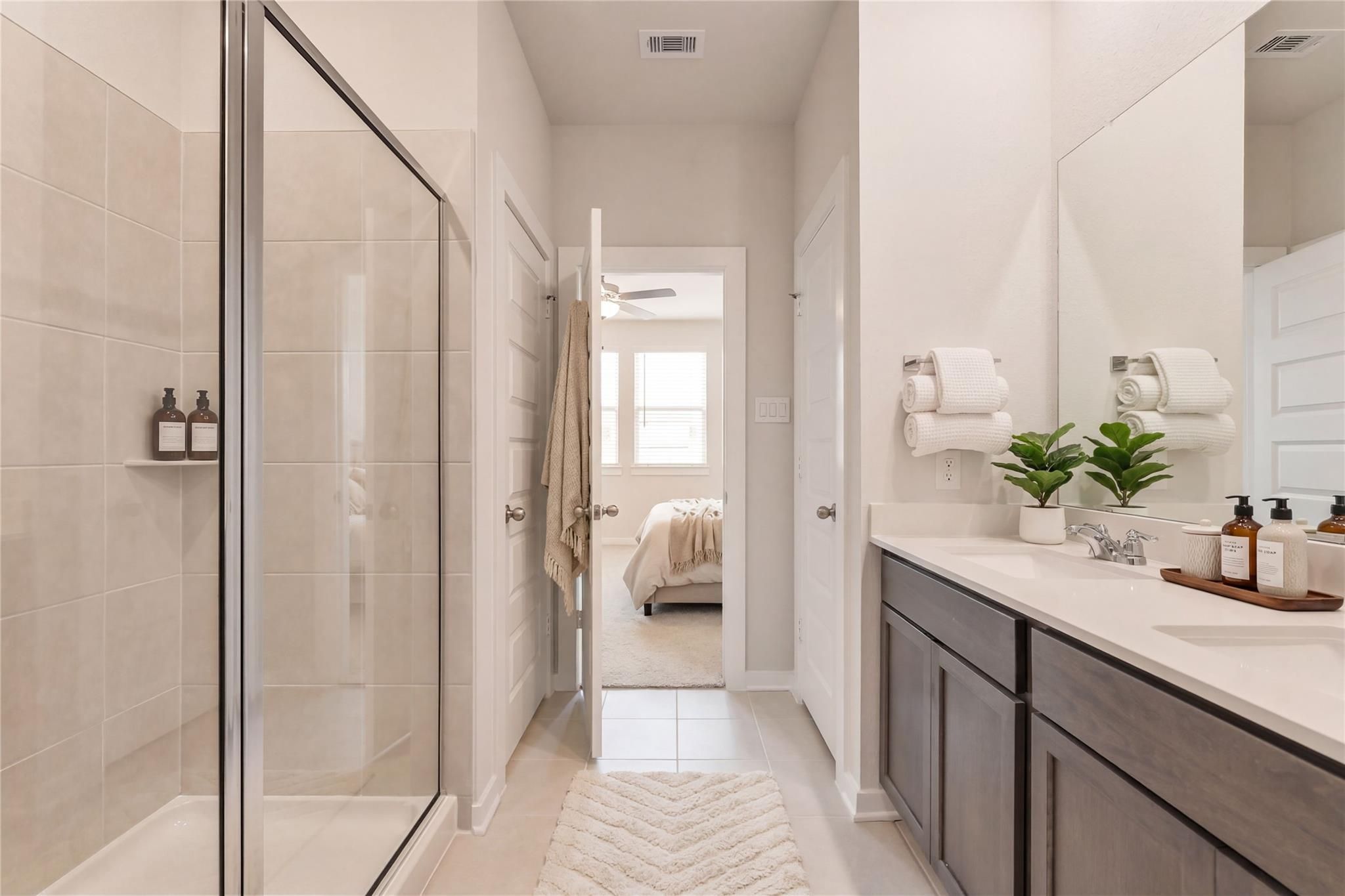 Modern master bathroom with frameless glass shower, double vanity, and adjoining bedroom in Davidson Homes The Brazos E, Cleveland, Texas