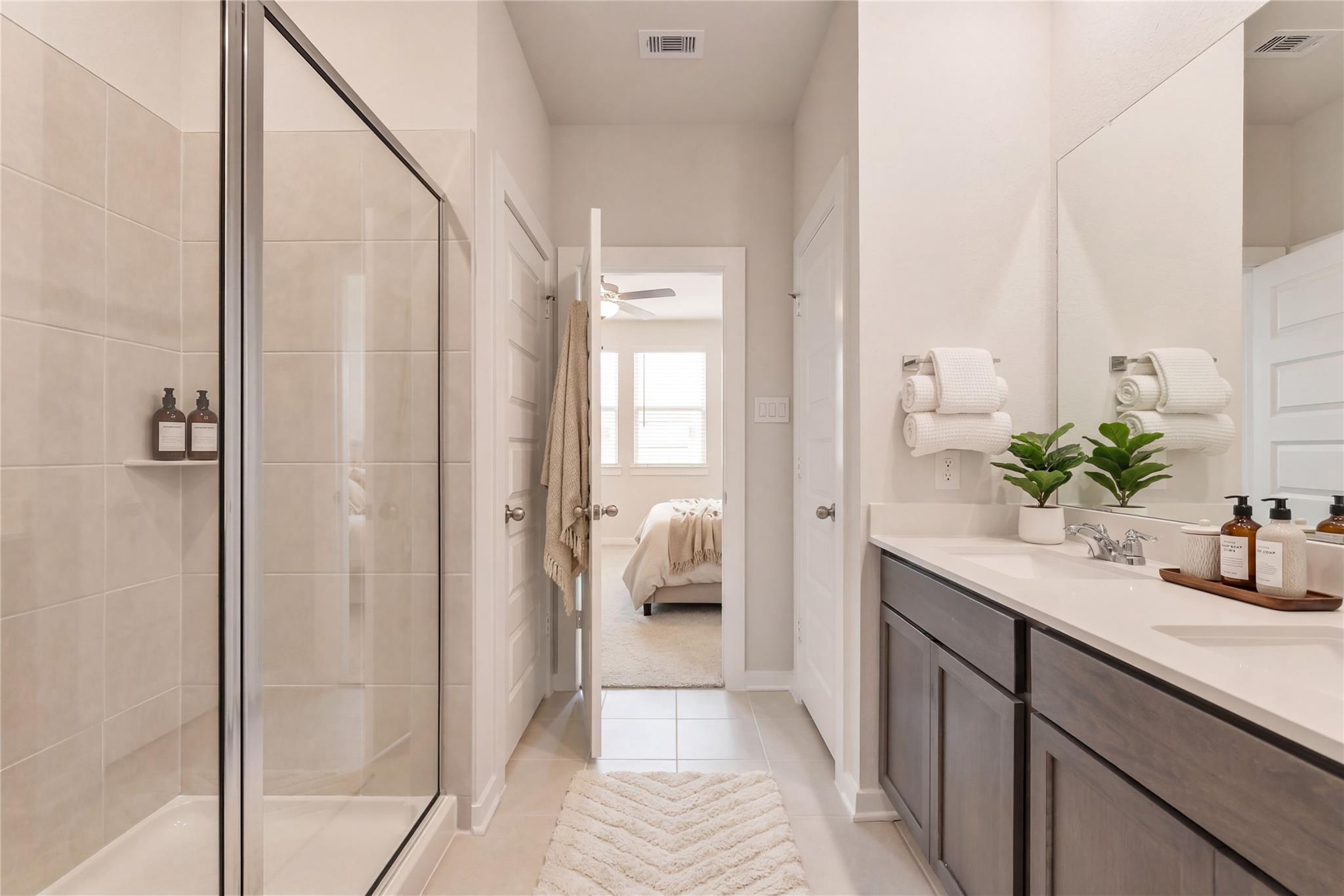 Modern master bathroom with frameless glass shower, double vanity, and adjoining bedroom in Davidson Homes The Brazos E, Cleveland, Texas
