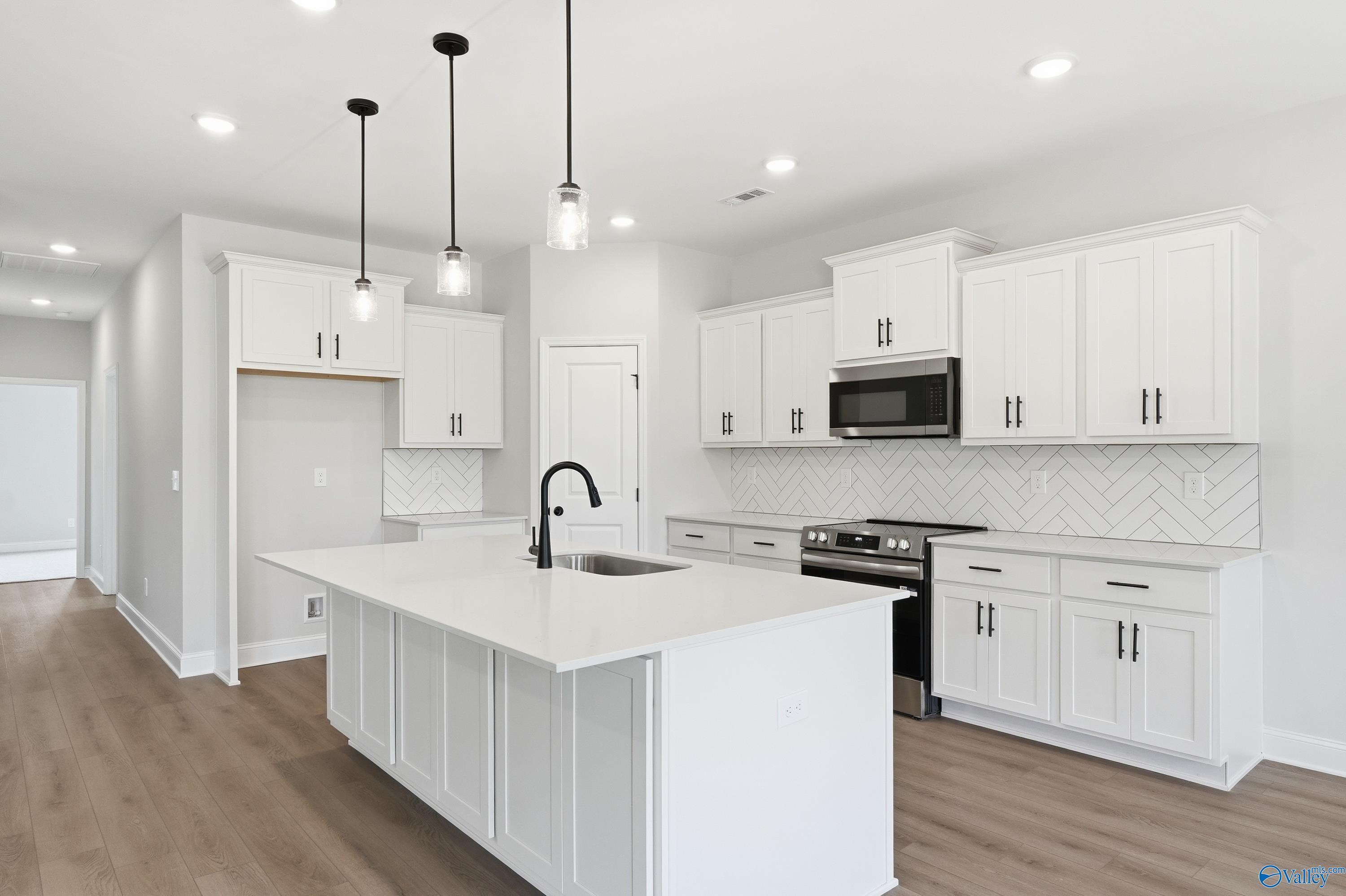 Modern white shaker kitchen with quartz island sink, stainless appliances, herringbone tile in Davidson Homes The Rockford C, Madison AL