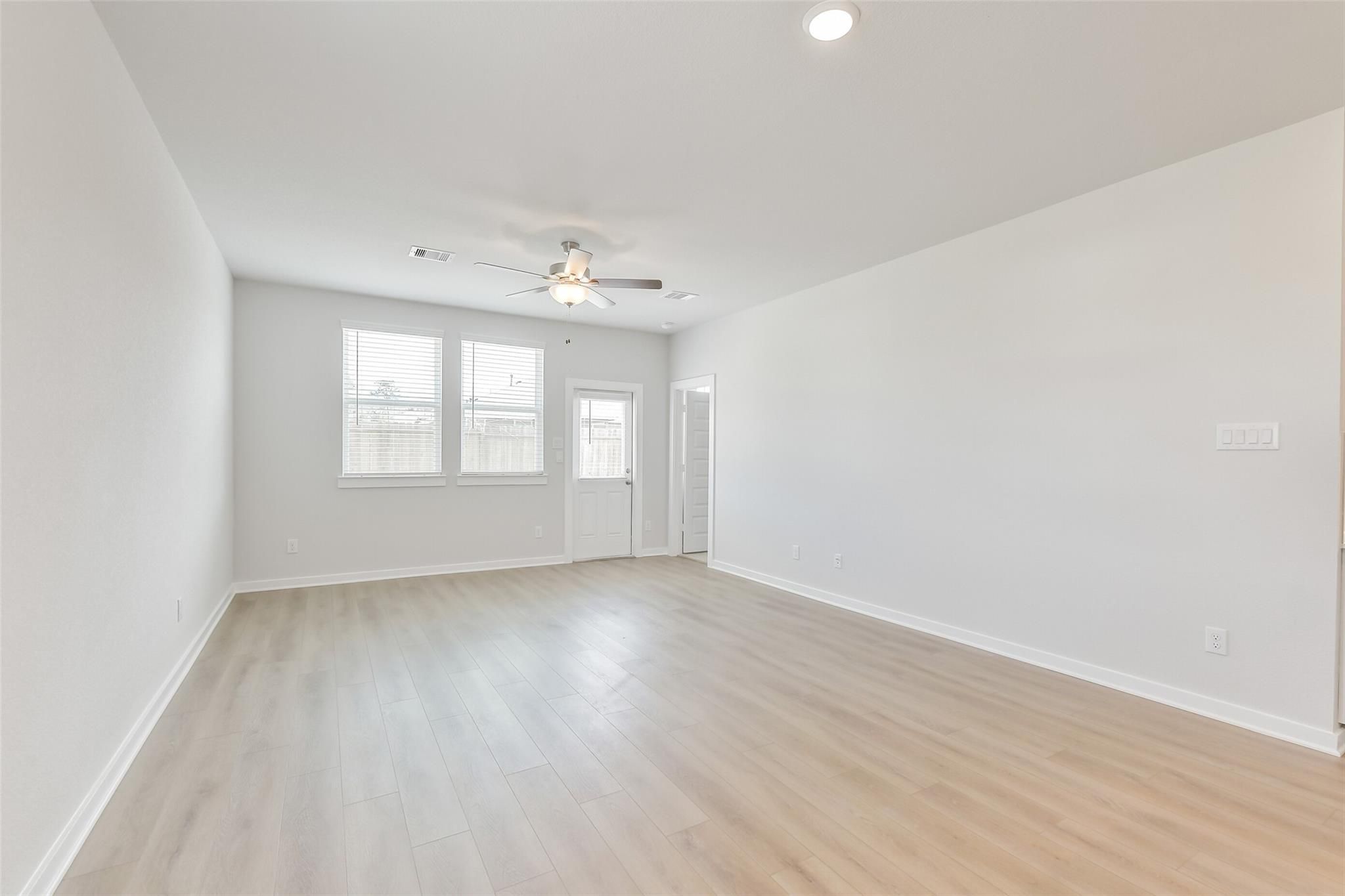 Spacious living room with light oak floors, large windows, ceiling fan in Davidson Homes The Colorado F, Cleveland TX
