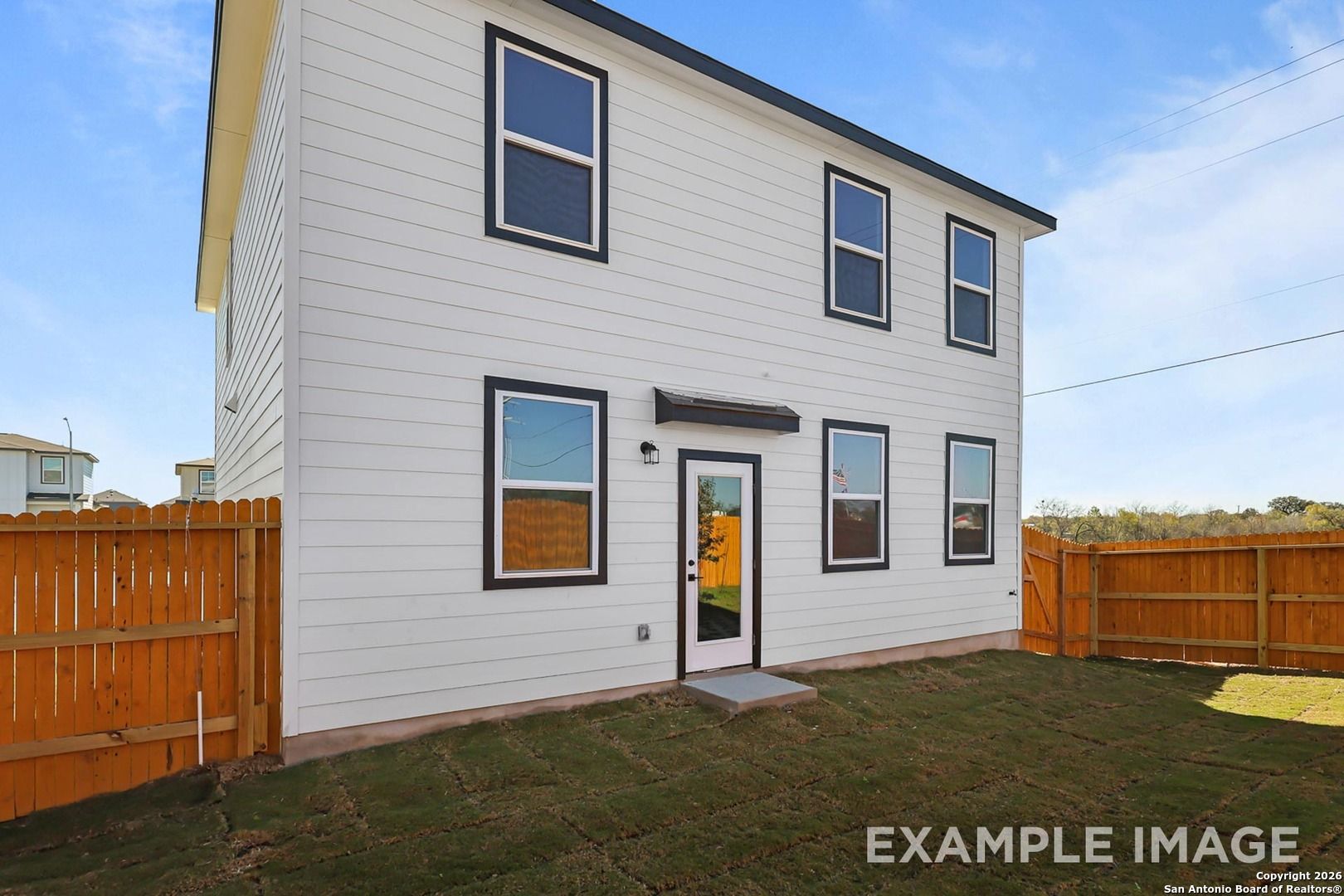 Two-story white home with black-trimmed windows, yellow door, and fenced grassy backyard in Applewhite Meadows, San Antonio, Texas - Davidson Homes The Trinity B