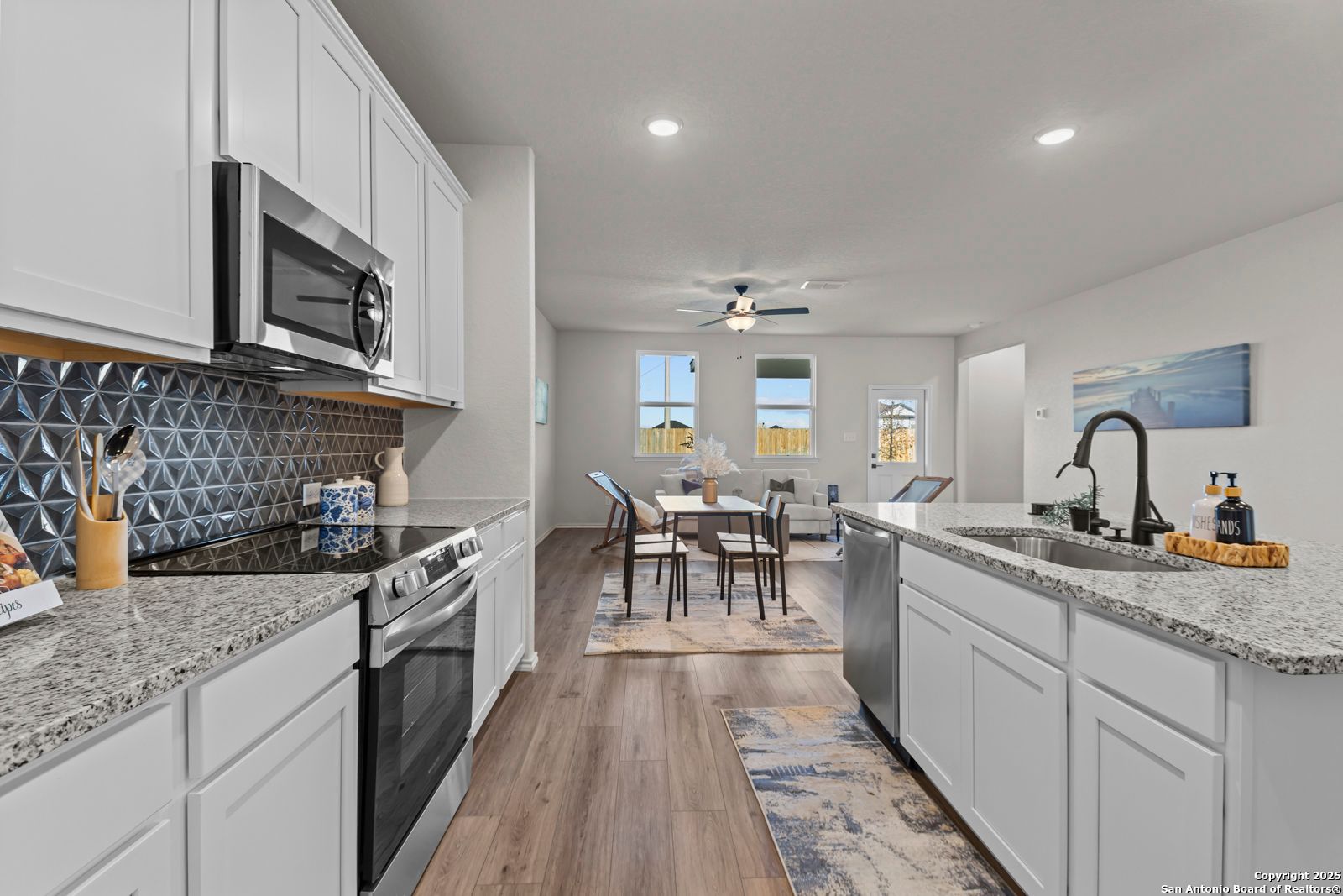 Open-concept kitchen with white cabinets, granite countertops, stainless appliances, and dining nook in The Douglas C home, Seguin, Texas