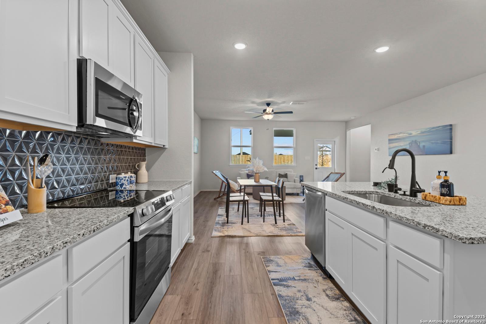 Open-concept kitchen with white cabinets, granite countertops, stainless appliances, and dining nook in The Douglas C home, Seguin, Texas