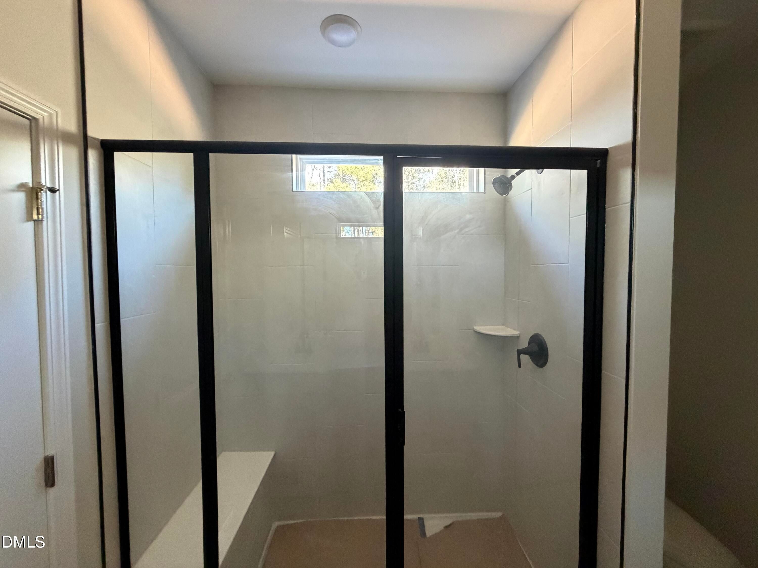 Modern glass-enclosed walk-in shower with bench seat, white tiles, and transom window in master bath of Davidson Homes The Carter C in Lillington, NC