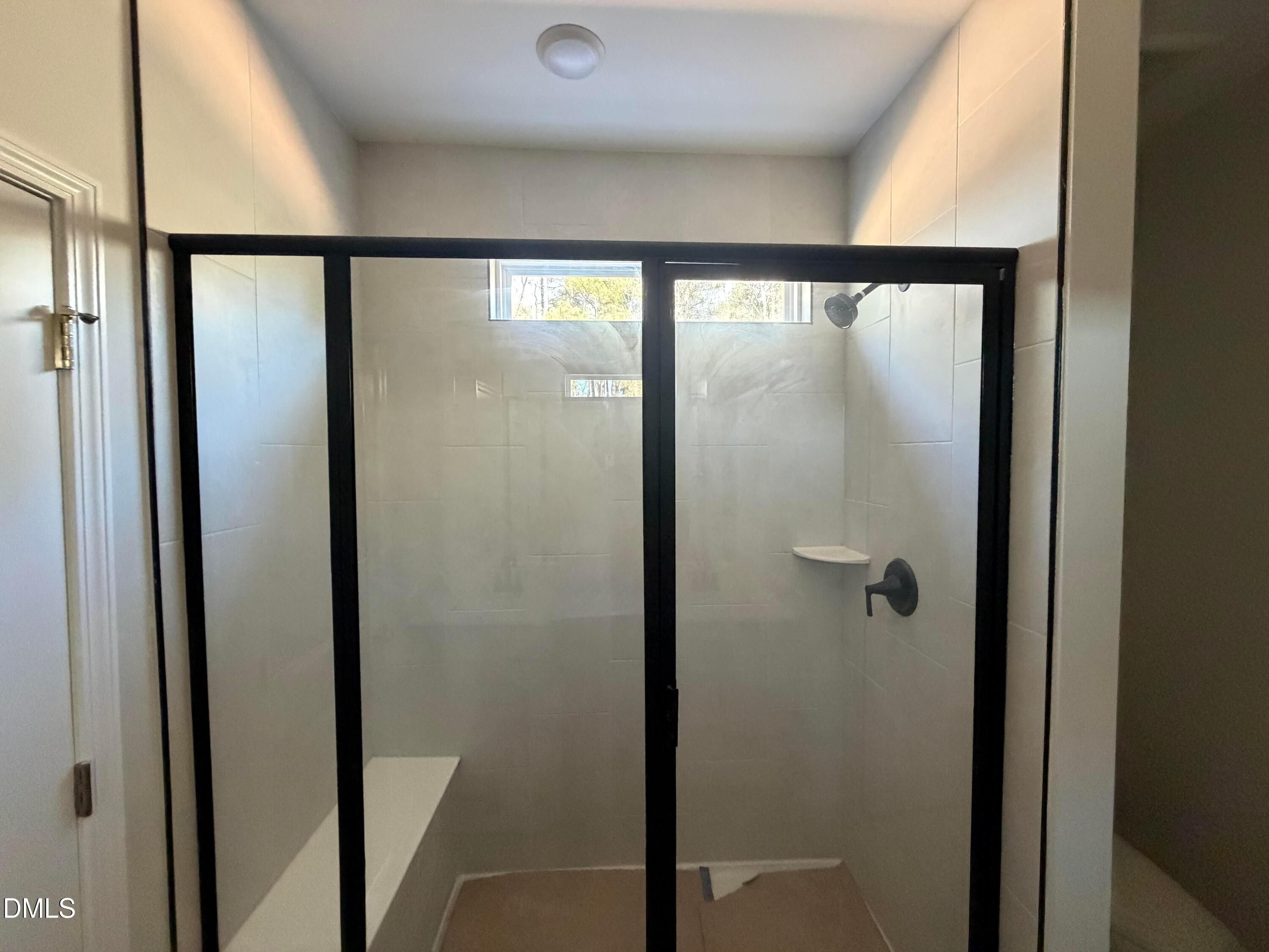 Modern glass-enclosed walk-in shower with bench seat, white tiles, and transom window in master bath of Davidson Homes The Carter C in Lillington, NC
