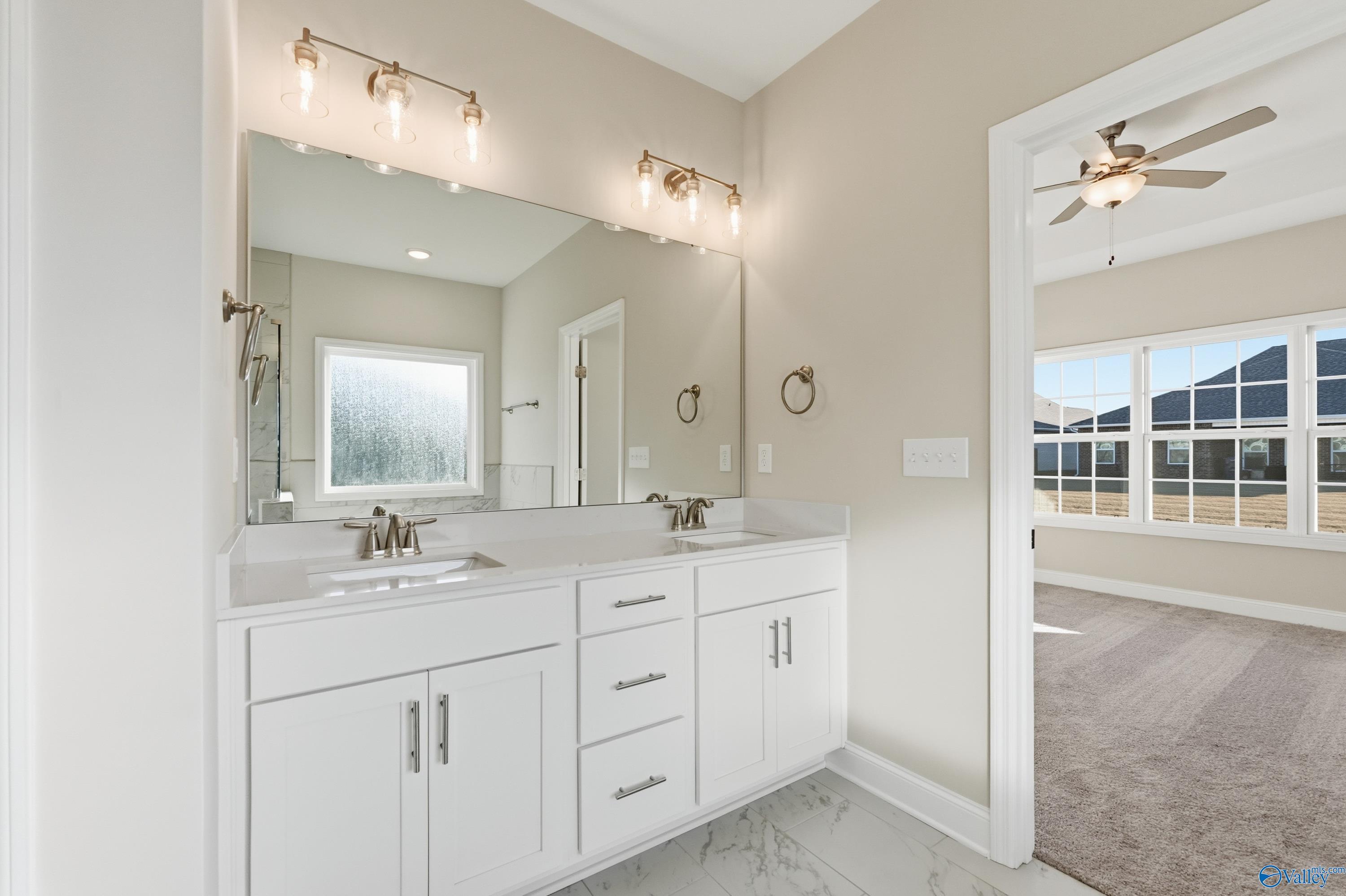 Modern master bathroom with double white vanity, sconce lighting, and open bedroom view in Davidson Homes The Montgomery B, Toney, AL