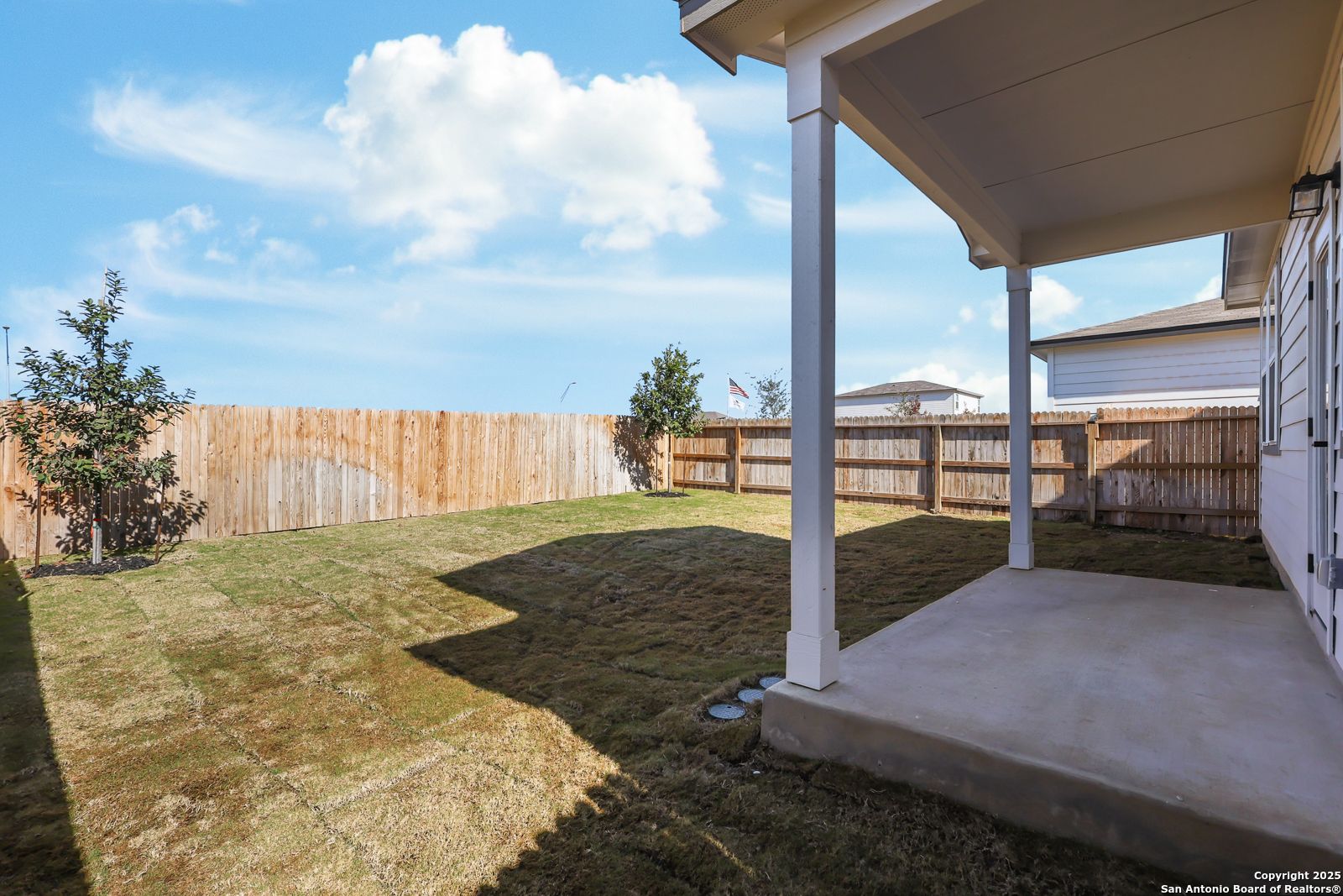 Covered back patio overlooking fenced grassy yard with young trees in Davidson Homes The Brazos C, Applewhite Meadows, San Antonio