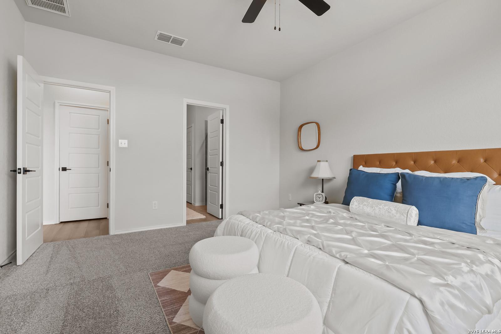 Elegant master bedroom with king bed, orange headboard, blue pillows, and open en-suite door in Davidson Homes The Daphne H, Seguin, Texas