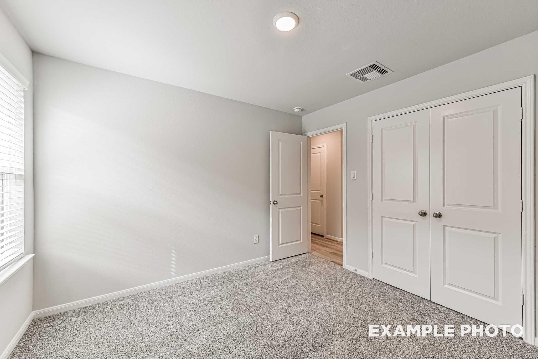 Spacious secondary bedroom with gray carpet, double closet doors, and window blinds in Davidson Homes The Riviera A, Rosharon, Texas