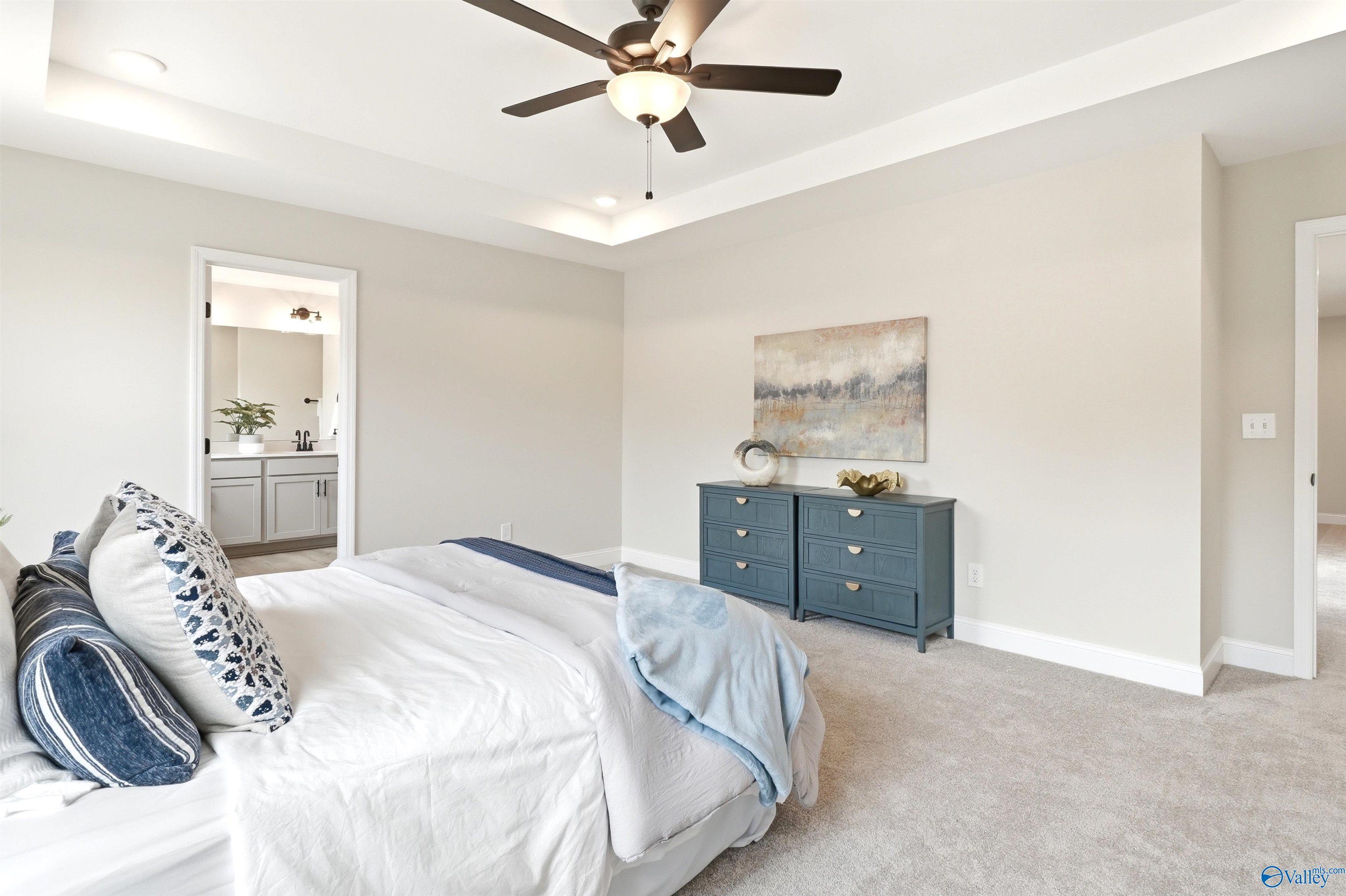 Bright primary bedroom with tray ceiling, ceiling fan, and blue accents in Davidson Homes The Russell A, Huntsville, AL