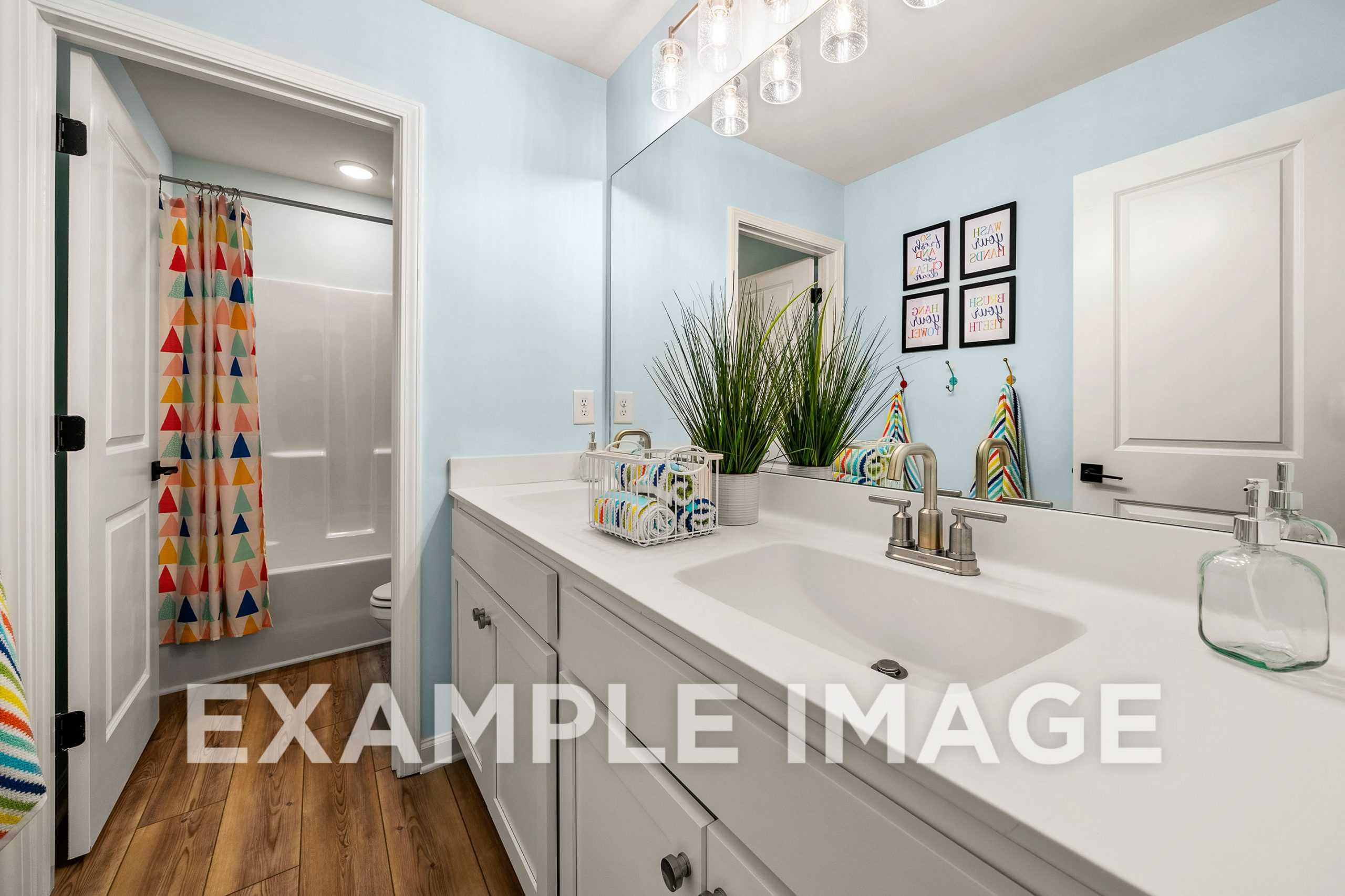 Vibrant bathroom in The Hickory A home featuring light blue walls, white vanity, colorful geometric shower curtain, and potted plant