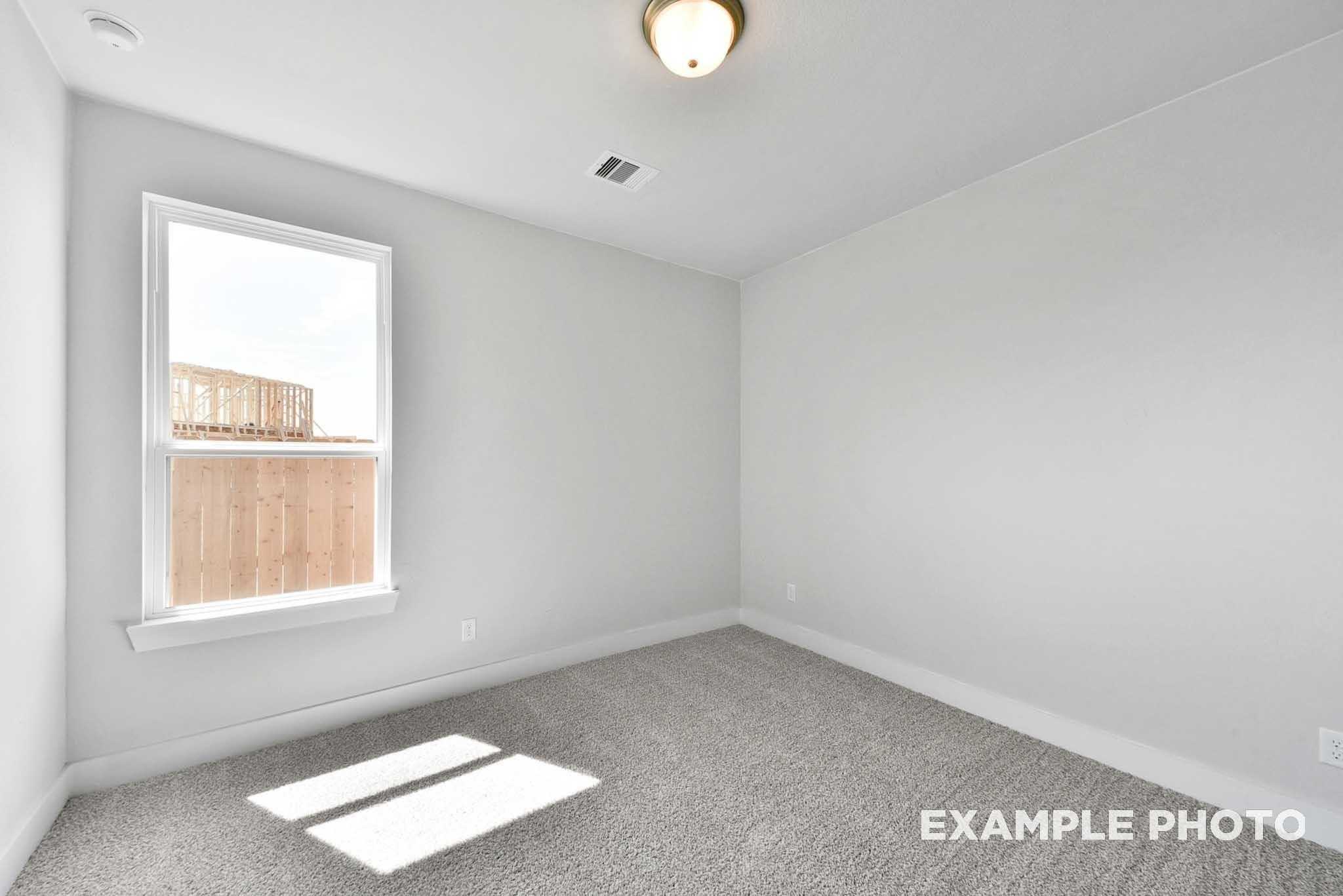 Bright empty bedroom with large window overlooking fenced yard, carpeted floor in Davidson Homes The George A, Texas City