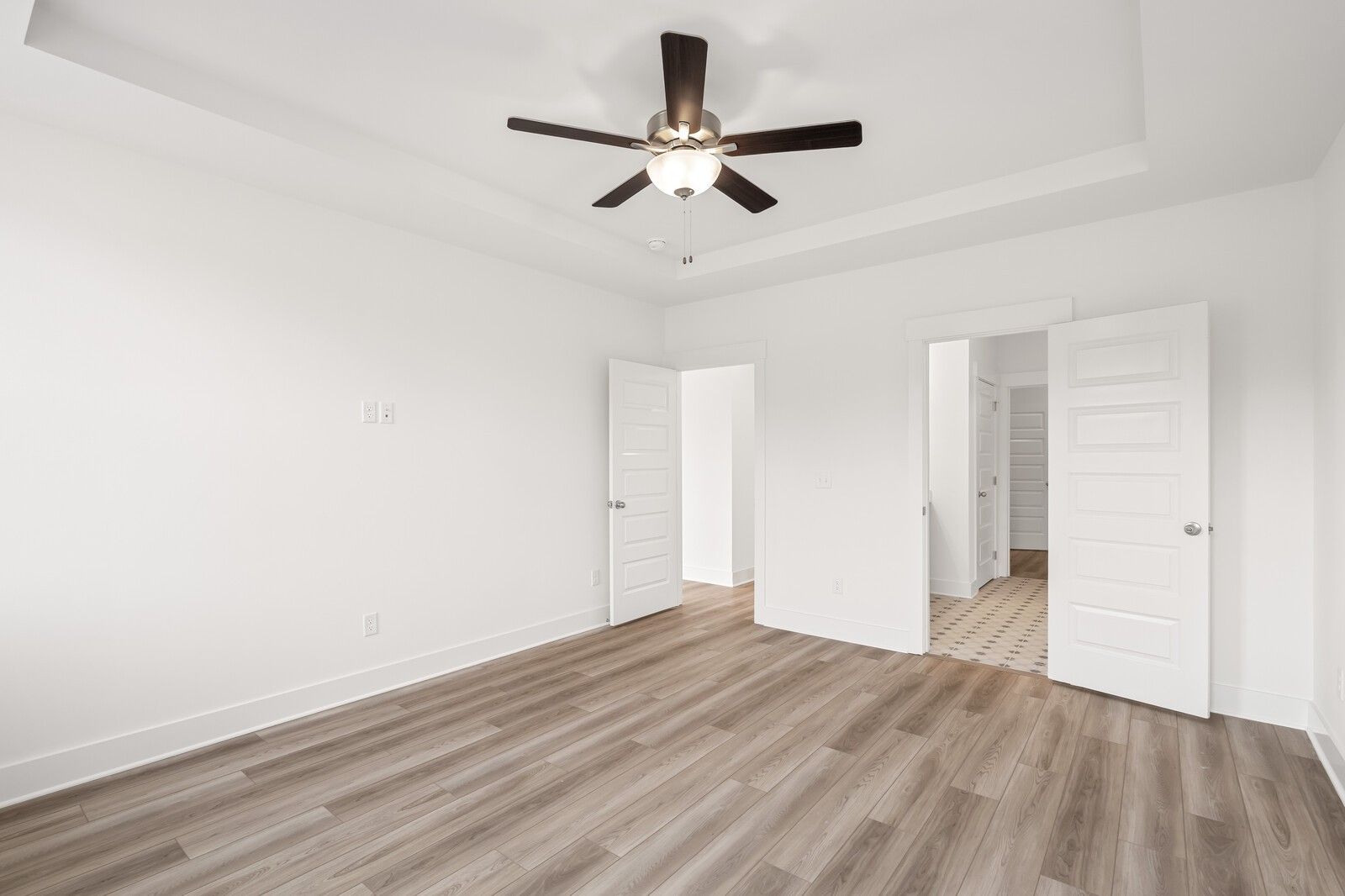 Bright bedroom with tray ceiling, ceiling fan, open doors to en-suite bath, hardwood floors in Davidson Homes The Ash C, Mt. Juliet, TN