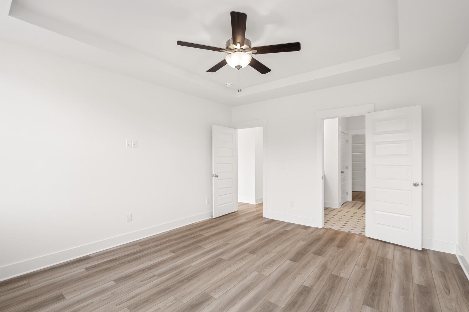 Bright bedroom with tray ceiling, ceiling fan, open doors to en-suite bath, hardwood floors in Davidson Homes The Ash C, Mt. Juliet, TN