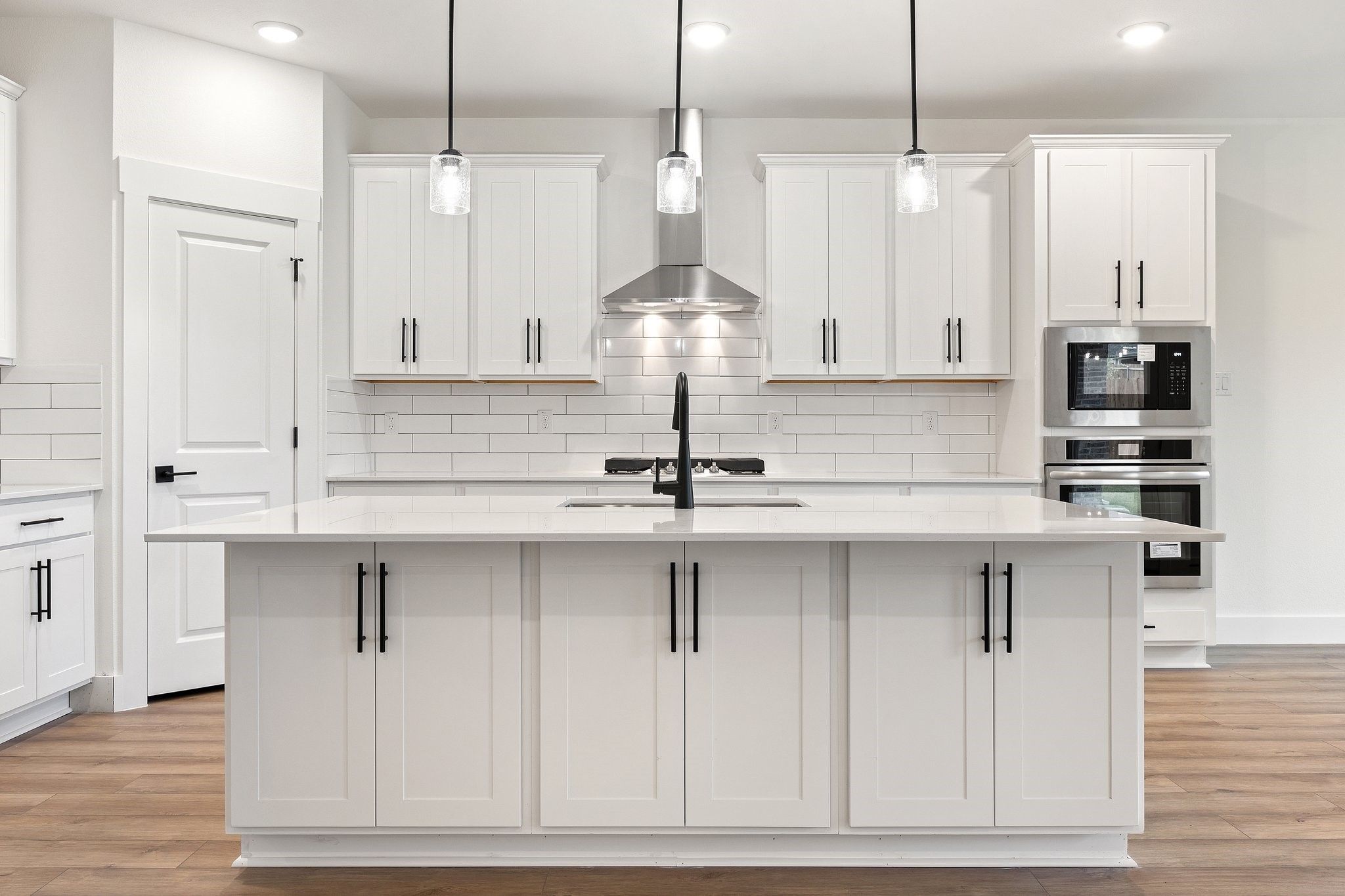 Modern white kitchen with quartz island, stainless appliances, and subway tile in The Rockford C plan, Josephine, Texas.