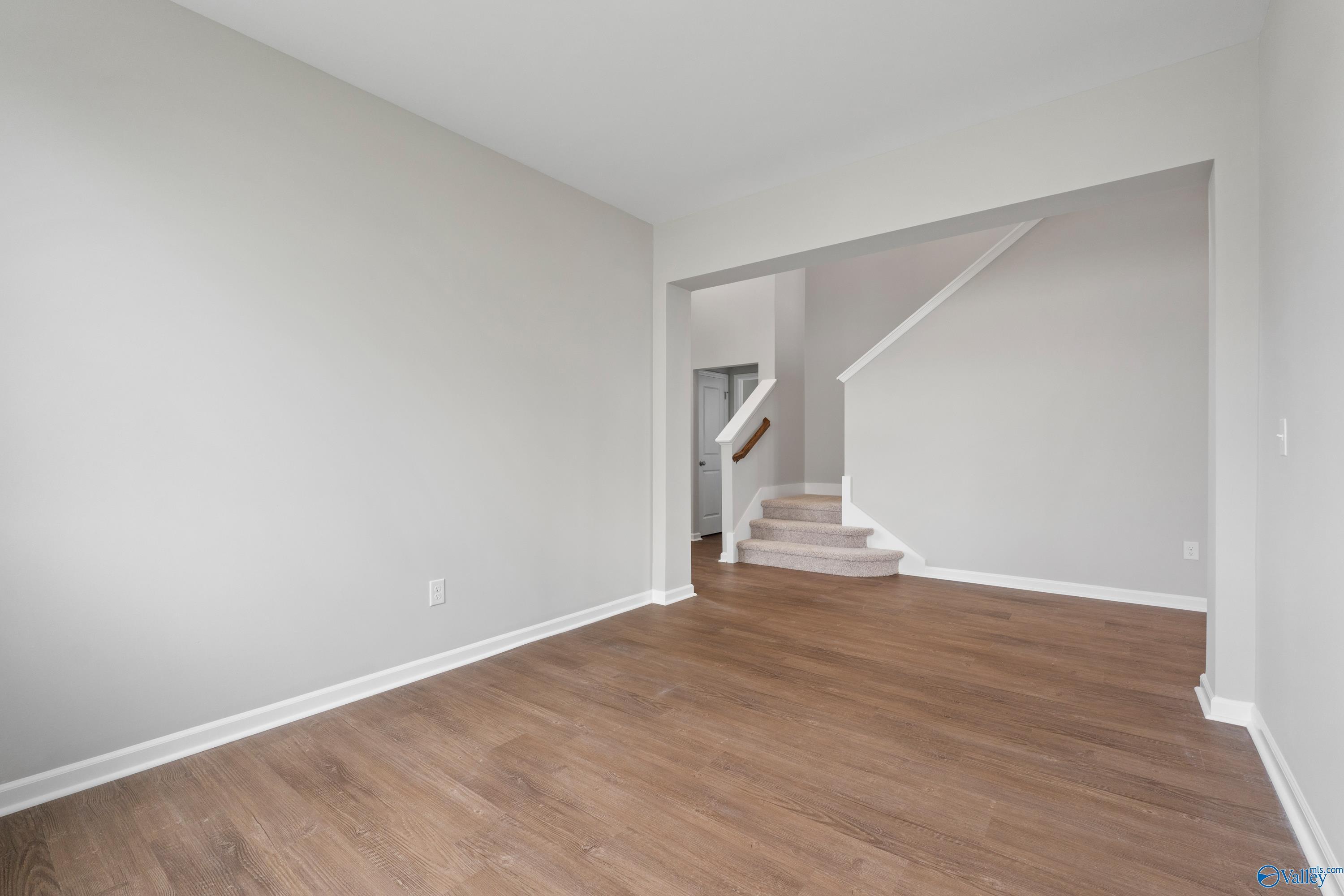 Bright entryway with light gray walls, hardwood floors, and open white staircase in Davidson Homes The Dorado, Athens Alabama