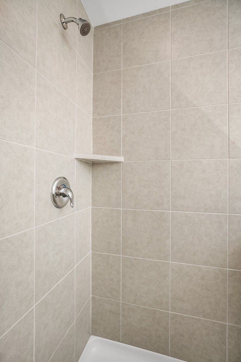 Modern tiled shower enclosure with chrome showerhead, faucet, and corner shelf in Davidson Homes The Gordon C, White House TN