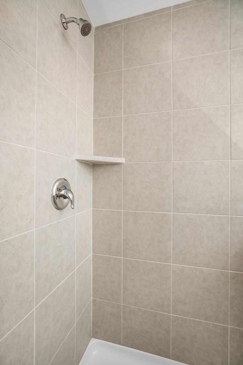 Modern tiled shower enclosure with chrome showerhead, faucet, and corner shelf in Davidson Homes The Gordon C, White House TN