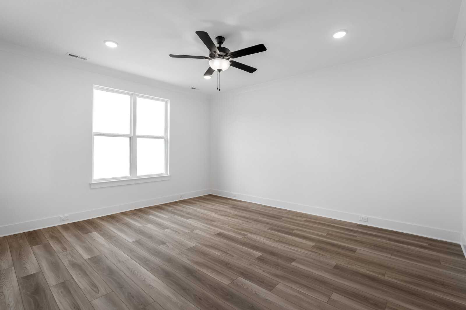 Bright bedroom with hardwood floors, ceiling fan, and large window in Davidson Homes The Hathaway, Murfreesboro, TN